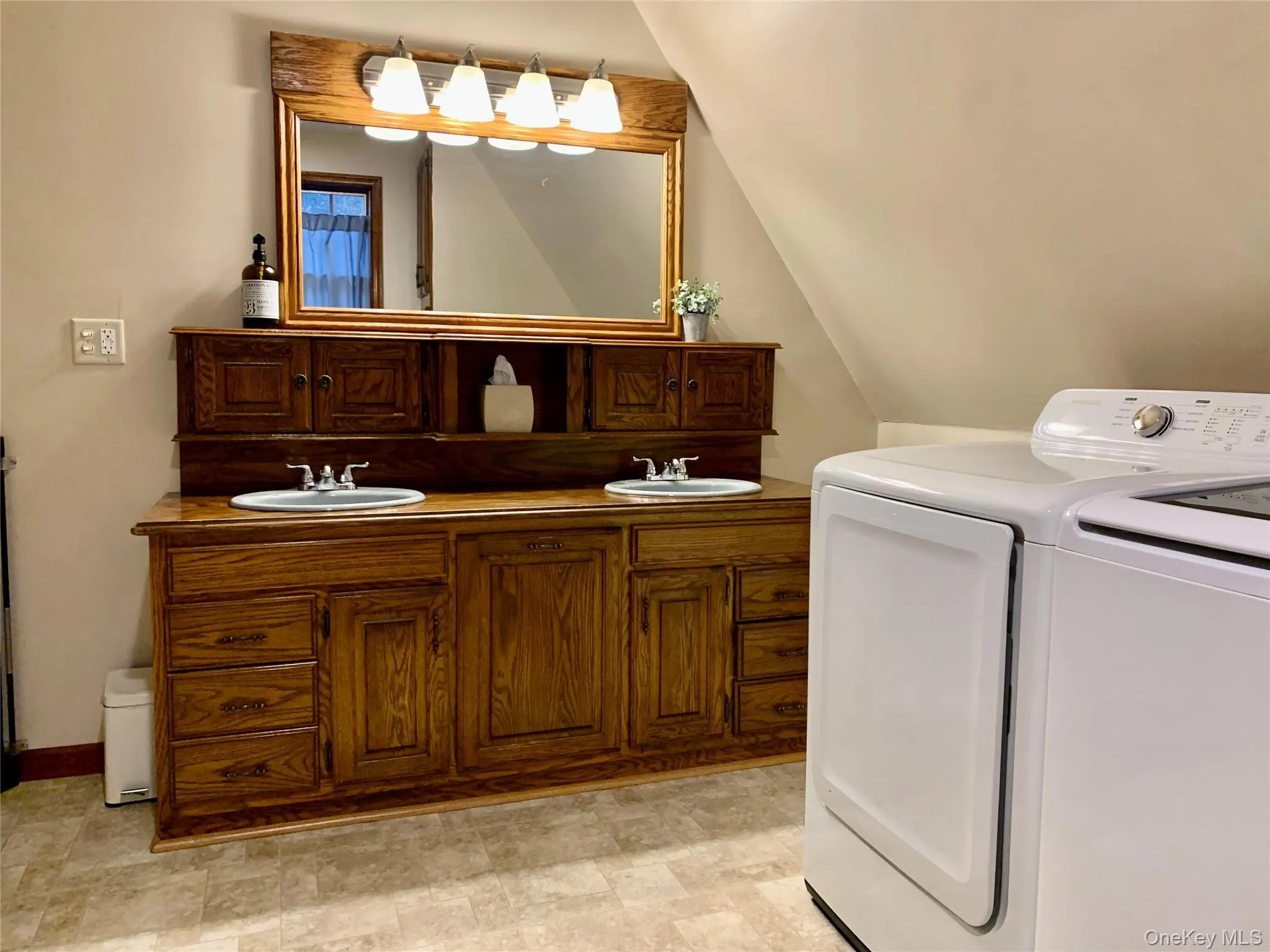 Full bathroom with double vanity, independent washer and dryer, vaulted ceiling, and stone finish flooring Full bathroom with double vanity, independent washer and dryer, vaulted ceiling, and stone finish flooring