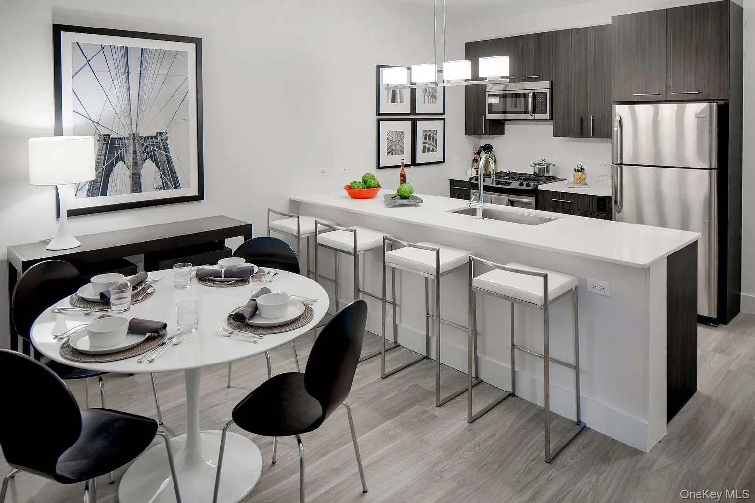 Kitchen featuring a peninsula, stainless steel appliances, a kitchen bar, light wood-type flooring, and hanging light fixtures Kitchen featuring a peninsula, stainless steel appliances, a kitchen bar, light wood-type flooring, and hanging light fixtures