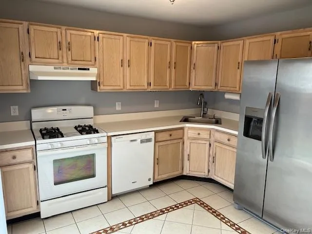 Kitchen with light brown cabinets, white appliances, light countertops, and light tile patterned flooring Kitchen with light brown cabinets, white appliances, light countertops, and light tile patterned flooring