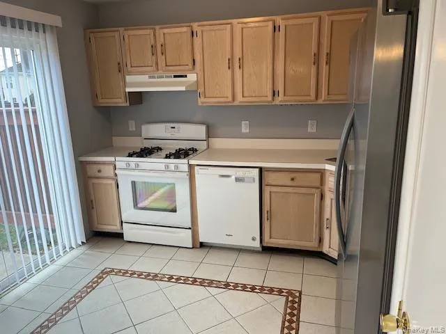Kitchen featuring light brown cabinets, white appliances, light countertops, light tile patterned flooring, and under cabinet range hood Kitchen featuring light brown cabinets, white appliances, light countertops, light tile patterned flooring, and under cabinet range hood