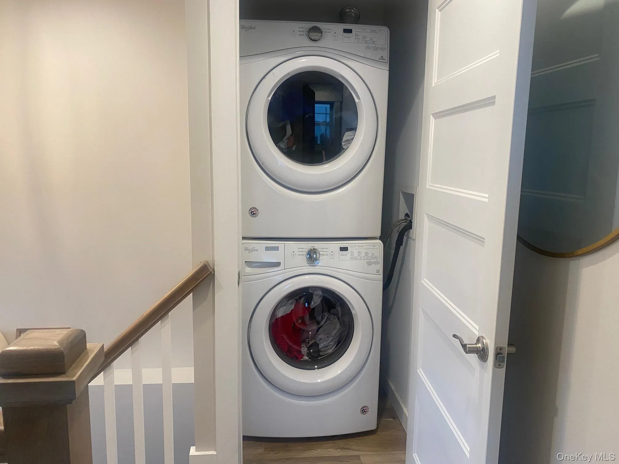 Washroom featuring stacked washer and clothes dryer and wood finished floors Washroom featuring stacked washer and clothes dryer and wood finished floors