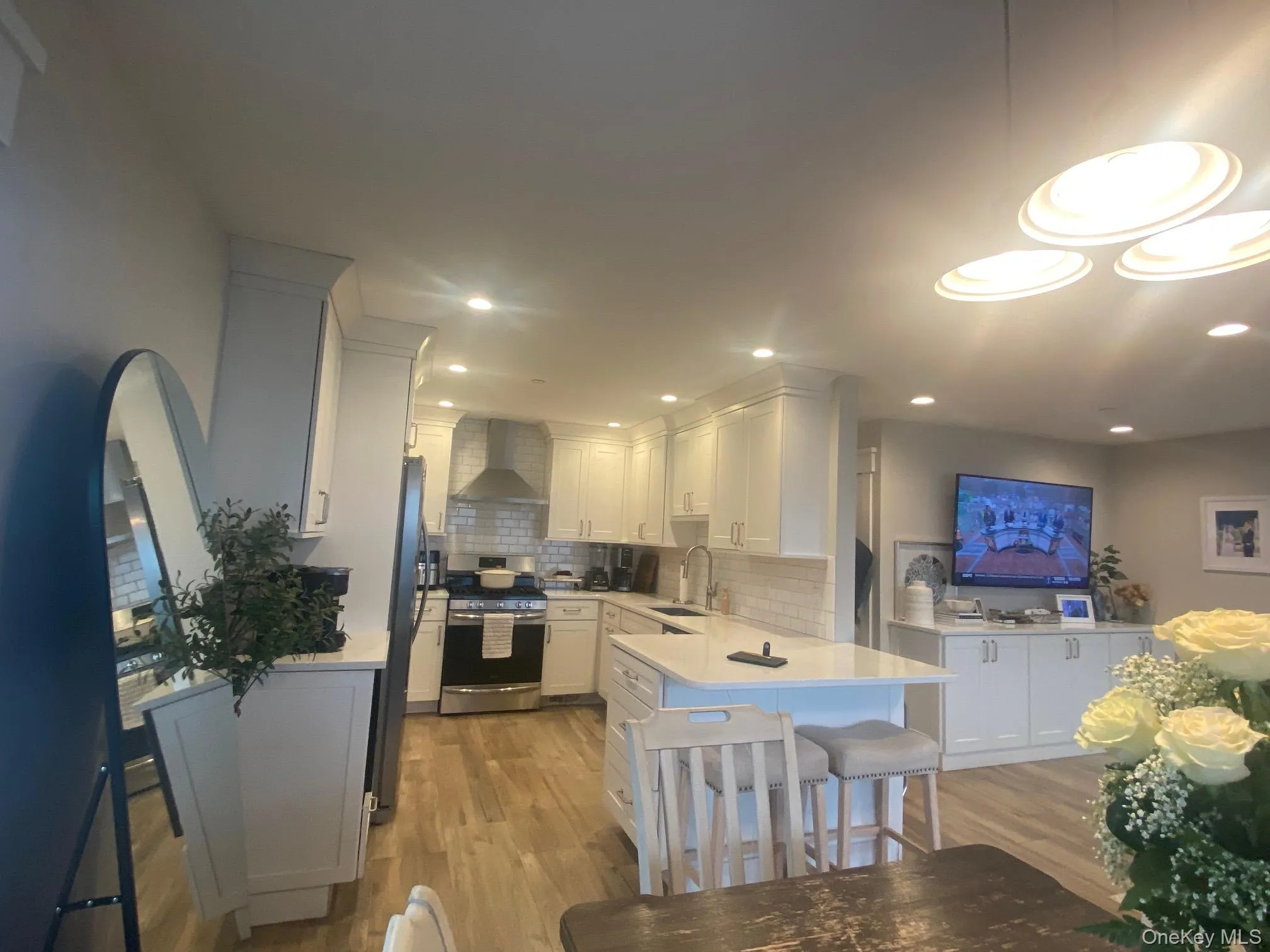 Kitchen featuring white cabinets, stainless steel appliances, wall chimney range hood, light wood finished floors, and a peninsula Kitchen featuring white cabinets, stainless steel appliances, wall chimney range hood, light wood finished floors, and a peninsula