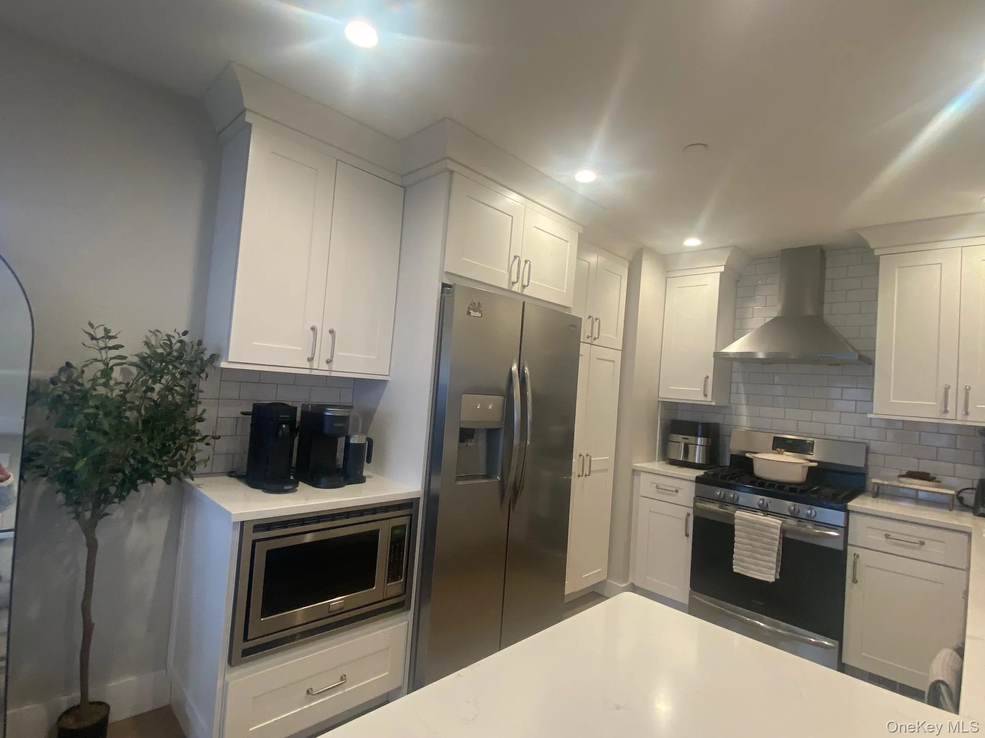 Kitchen with appliances with stainless steel finishes, wall chimney range hood, white cabinets, tasteful backsplash, and recessed lighting Kitchen with appliances with stainless steel finishes, wall chimney range hood, white cabinets, tasteful backsplash, and recessed lighting