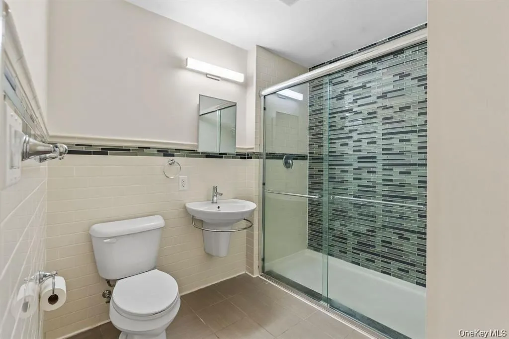 Bathroom with a shower stall, tile walls, tile patterned flooring, and a wainscoted wall Bathroom with a shower stall, tile walls, tile patterned flooring, and a wainscoted wall