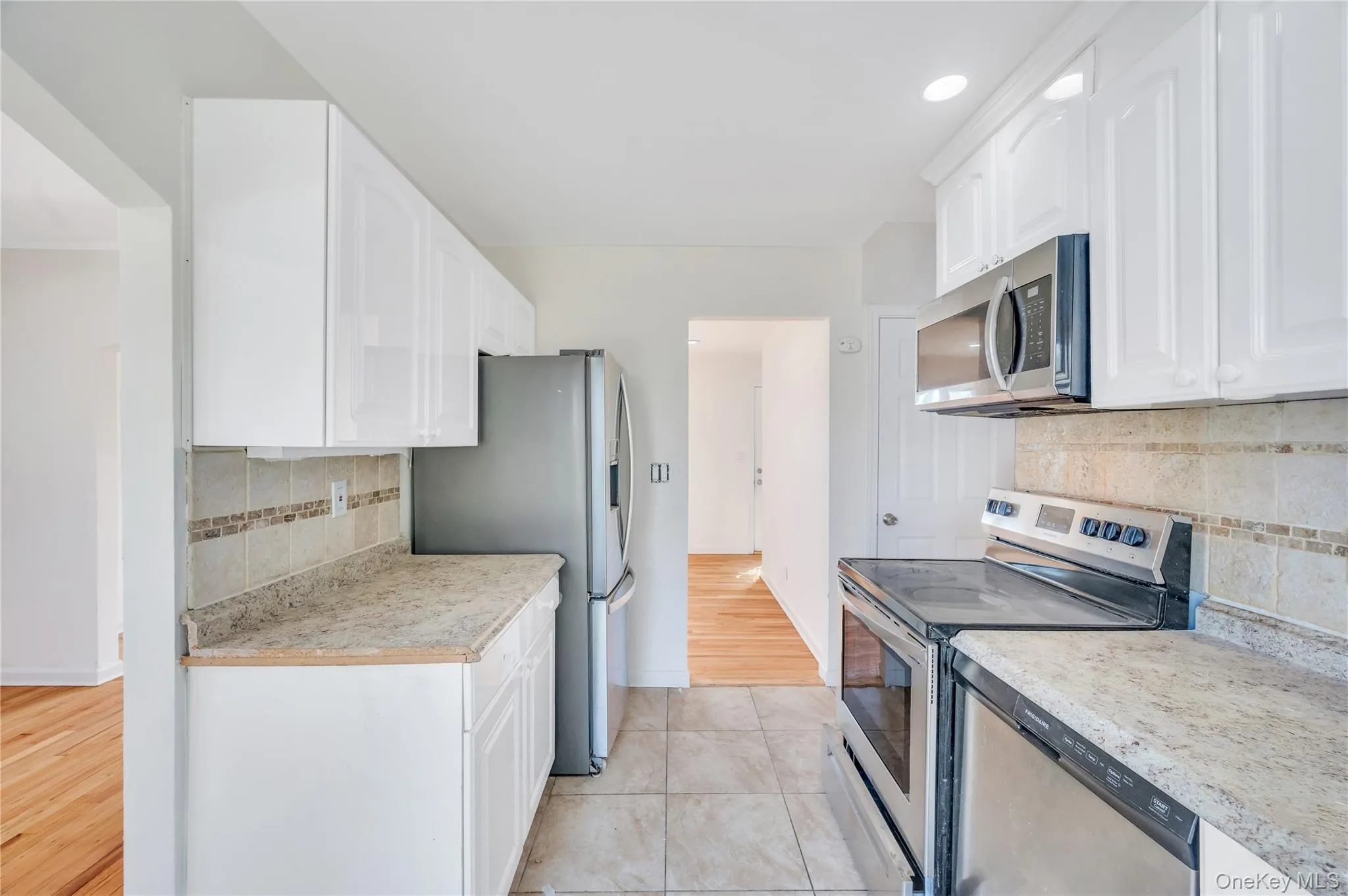 Kitchen with stainless steel appliances, tasteful backsplash, light countertops, white cabinetry, and light wood-style floors Kitchen with stainless steel appliances, tasteful backsplash, light countertops, white cabinetry, and light wood-style floors