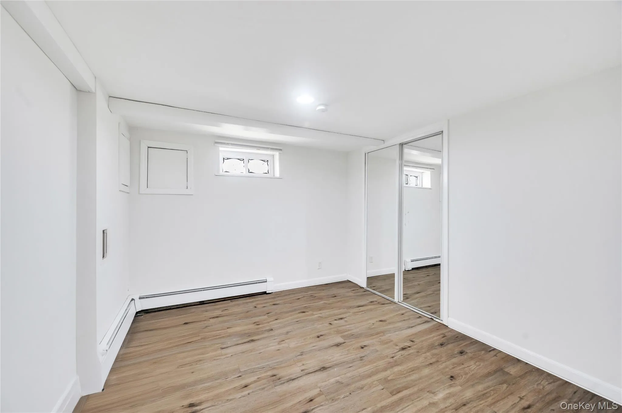 Below grade area featuring wood finished floors, baseboard heating, and a baseboard heating unit Below grade area featuring wood finished floors, baseboard heating, and a baseboard heating unit