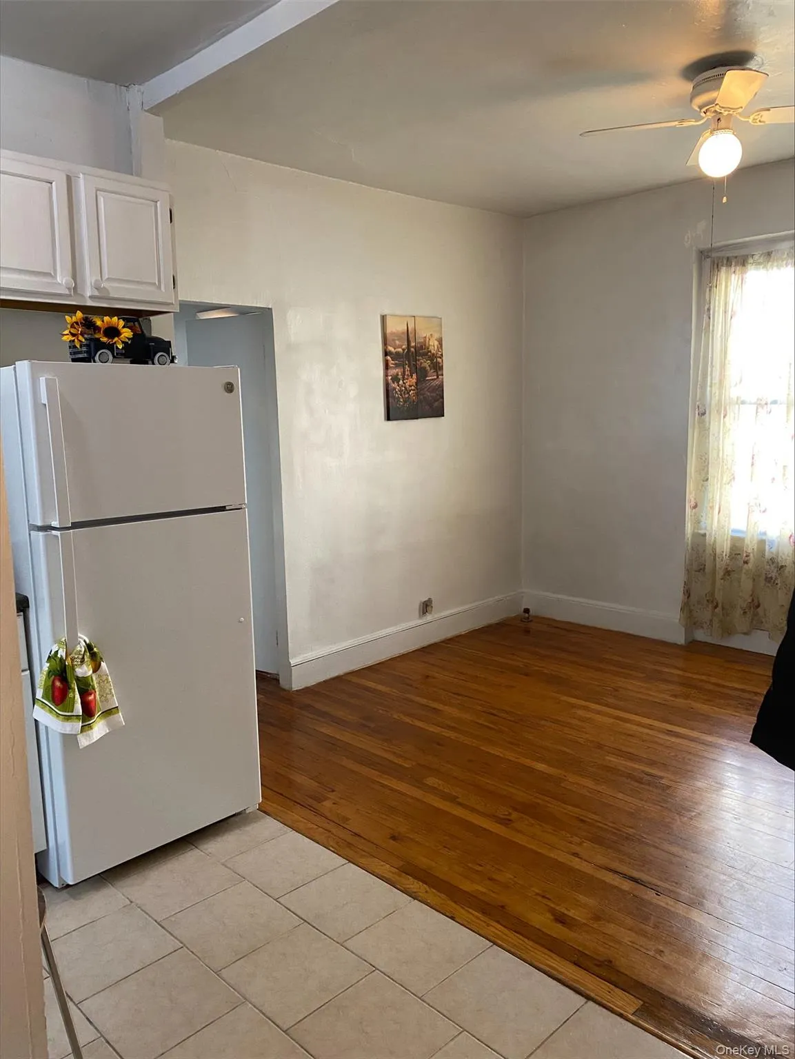 Kitchen featuring freestanding refrigerator, light tile patterned floors, a ceiling fan, and white cabinetry Kitchen featuring freestanding refrigerator, light tile patterned floors, a ceiling fan, and white cabinetry