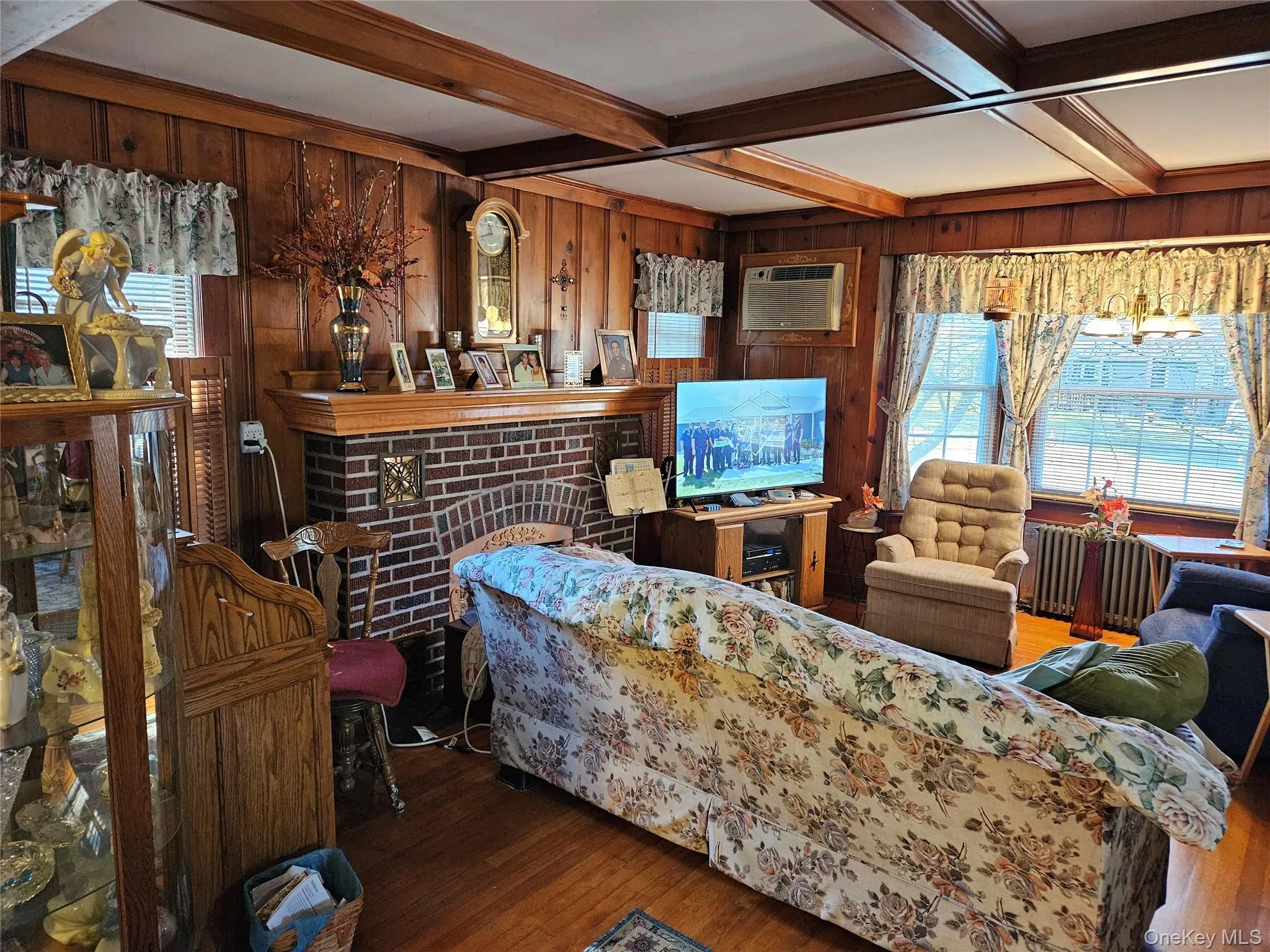 Living area featuring beamed ceiling, wood-type flooring, radiator, a fireplace, and wood walls Living area featuring beamed ceiling, wood-type flooring, radiator, a fireplace, and wood walls