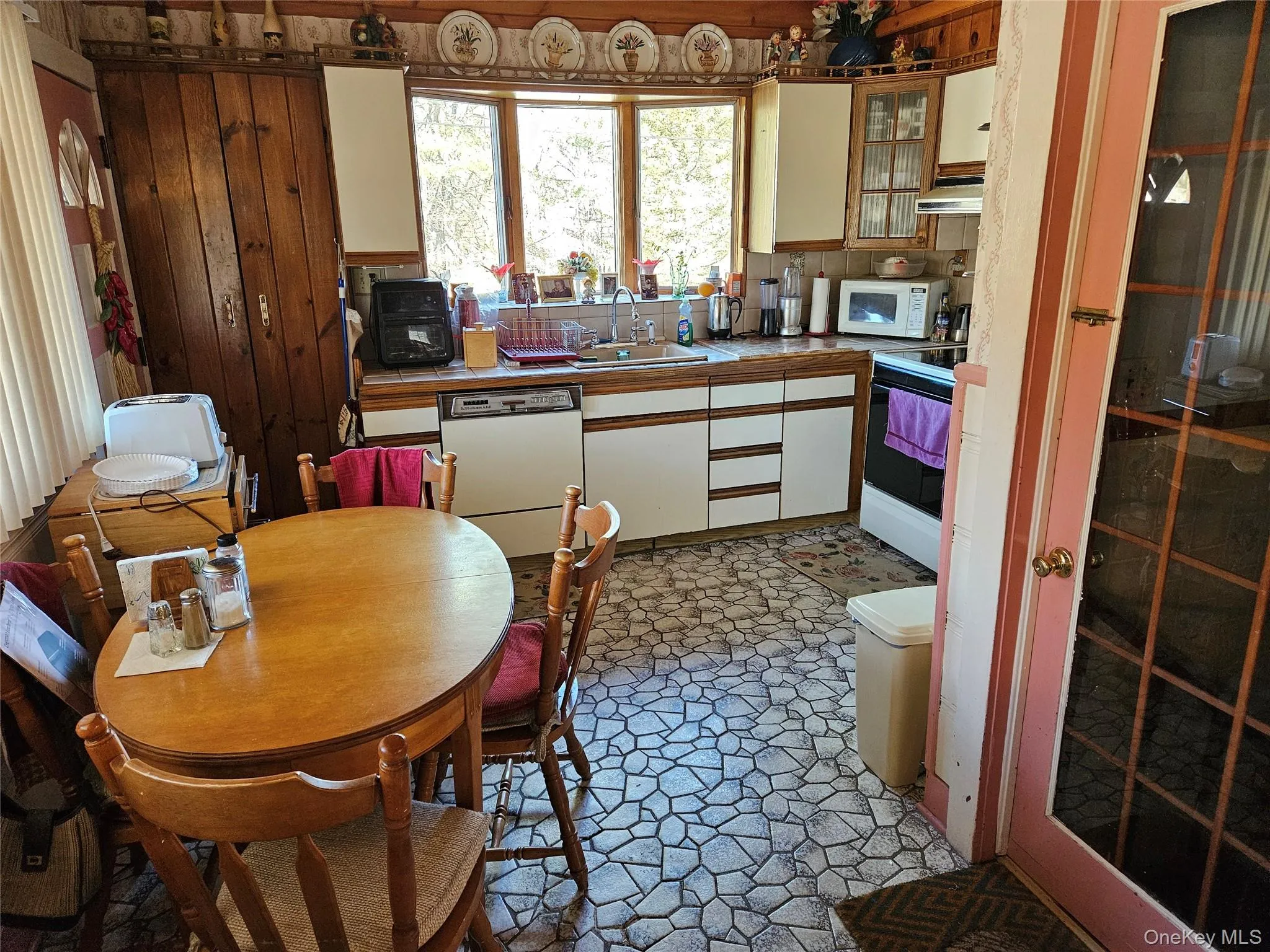 Kitchen featuring brown cabinets, white appliances, white cabinetry, light countertops, and under cabinet range hood Kitchen featuring brown cabinets, white appliances, white cabinetry, light countertops, and under cabinet range hood