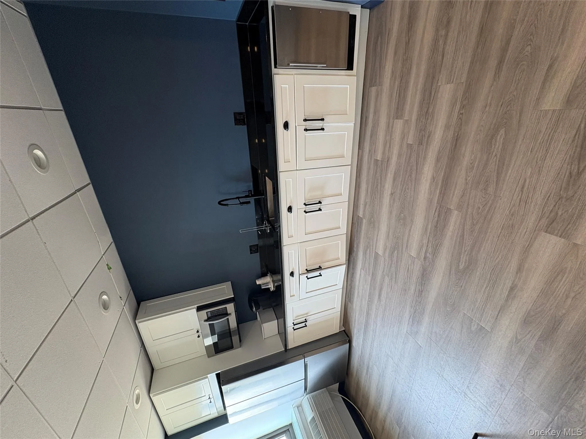 Kitchen featuring refrigerator, white cabinetry, a paneled ceiling, light wood-type flooring, and dark stone counters Kitchen featuring refrigerator, white cabinetry, a paneled ceiling, light wood-type flooring, and dark stone counters