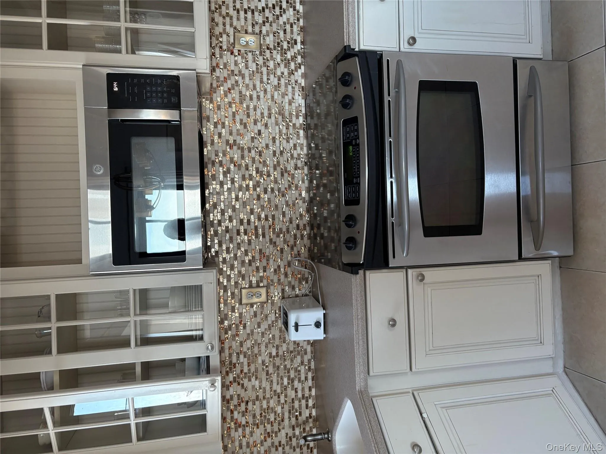 Kitchen with stainless steel appliances, glass insert cabinets, white cabinets, and light tile patterned flooring Kitchen with stainless steel appliances, glass insert cabinets, white cabinets, and light tile patterned flooring