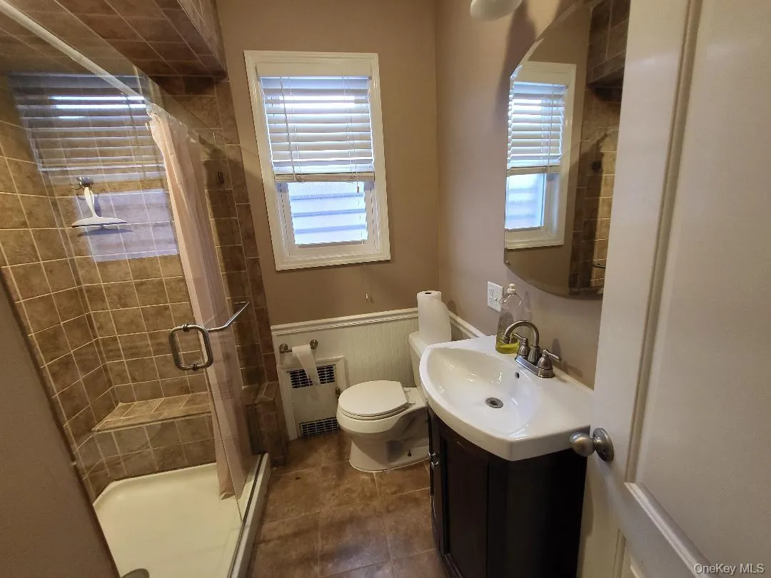 Full bathroom featuring vanity, a stall shower, wainscoting, radiator heating unit, and baseboard heating Full bathroom featuring vanity, a stall shower, wainscoting, radiator heating unit, and baseboard heating