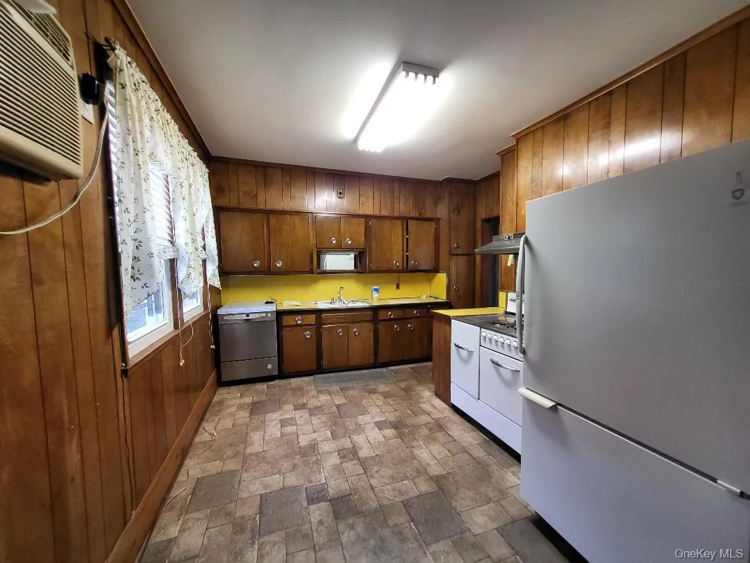 Kitchen featuring freestanding refrigerator, wood walls, stone finish flooring, range with two ovens, and dishwasher Kitchen featuring freestanding refrigerator, wood walls, stone finish flooring, range with two ovens, and dishwasher