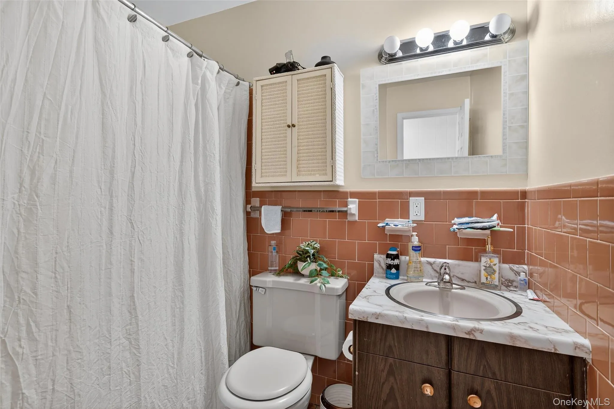 Full bath featuring vanity, tile walls, a wainscoted wall, and curtained shower Full bath featuring vanity, tile walls, a wainscoted wall, and curtained shower