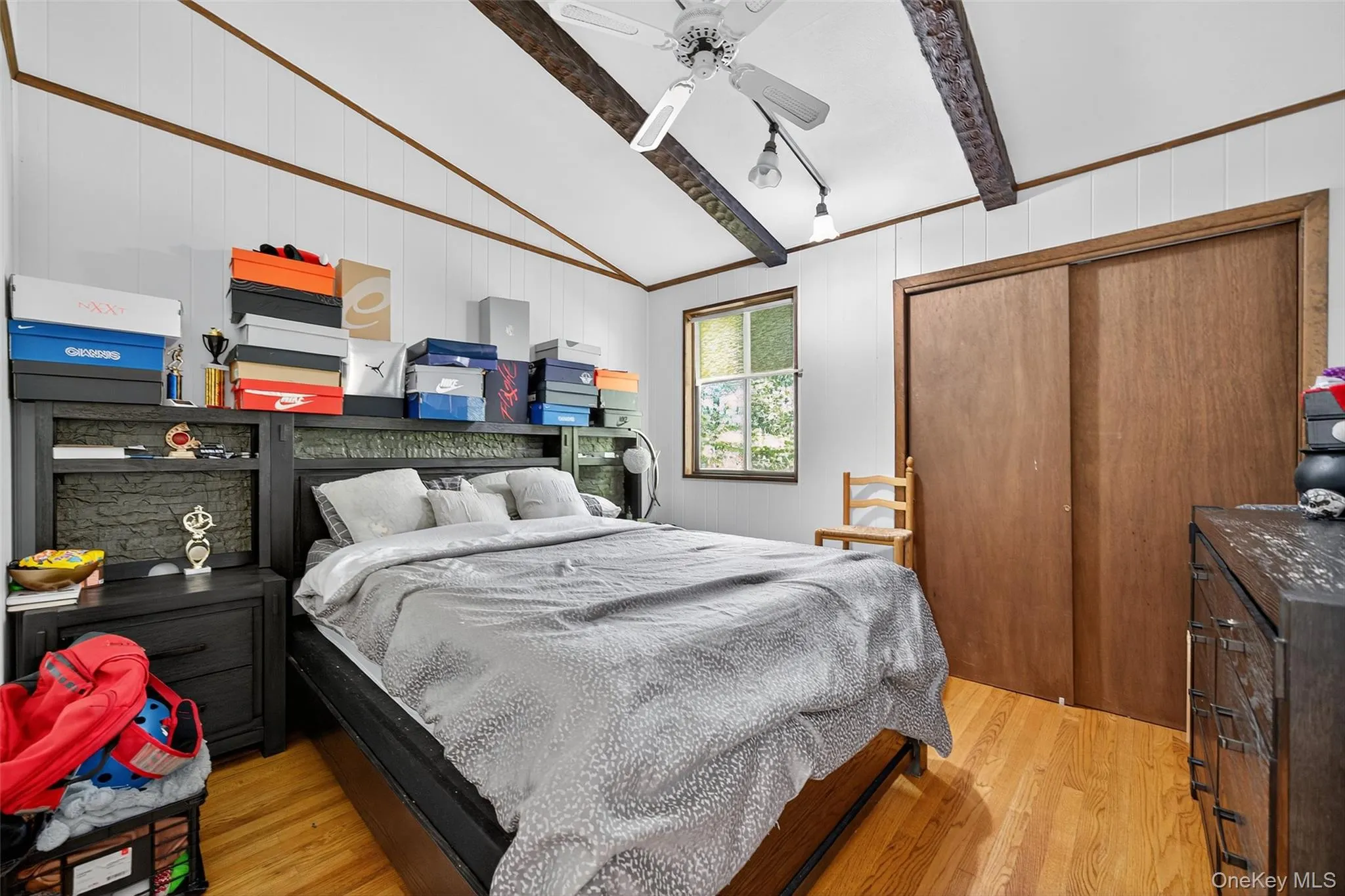 Bedroom with light wood finished floors, a closet, wood walls, and a ceiling fan Bedroom with light wood finished floors, a closet, wood walls, and a ceiling fan