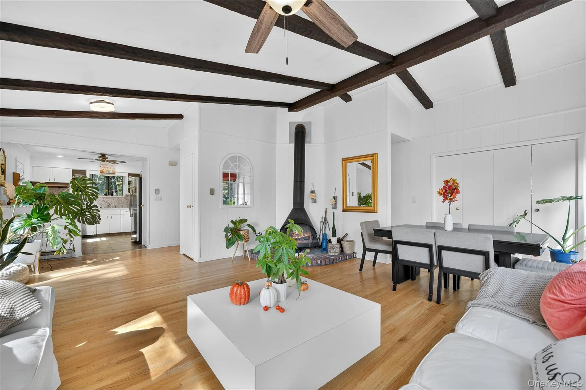 Living area with a ceiling fan, a wood stove, light wood-style flooring, and beamed ceiling Living area with a ceiling fan, a wood stove, light wood-style flooring, and beamed ceiling