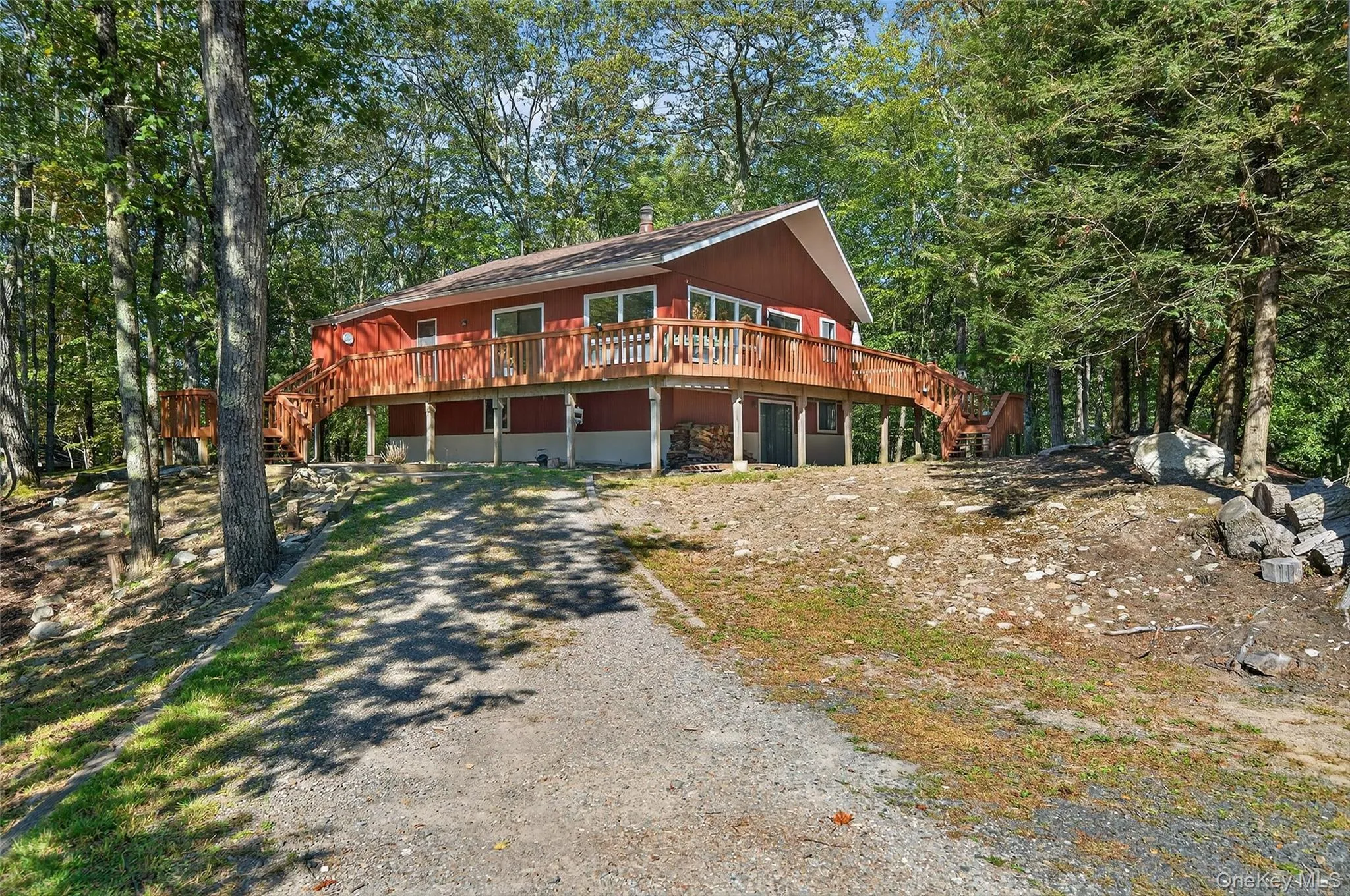 Rustic home featuring a wooden deck, stairway, gravel driveway, and a wooded view Rustic home featuring a wooden deck, stairway, gravel driveway, and a wooded view