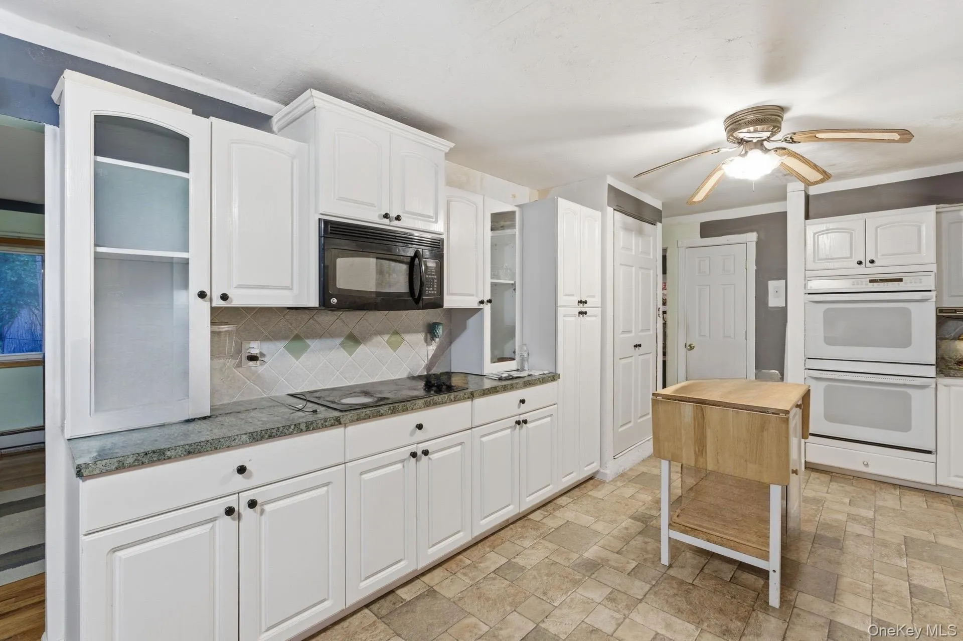 Kitchen featuring stone finish floors, black appliances, white cabinetry, ceiling fan, and decorative backsplash Kitchen featuring stone finish floors, black appliances, white cabinetry, ceiling fan, and decorative backsplash