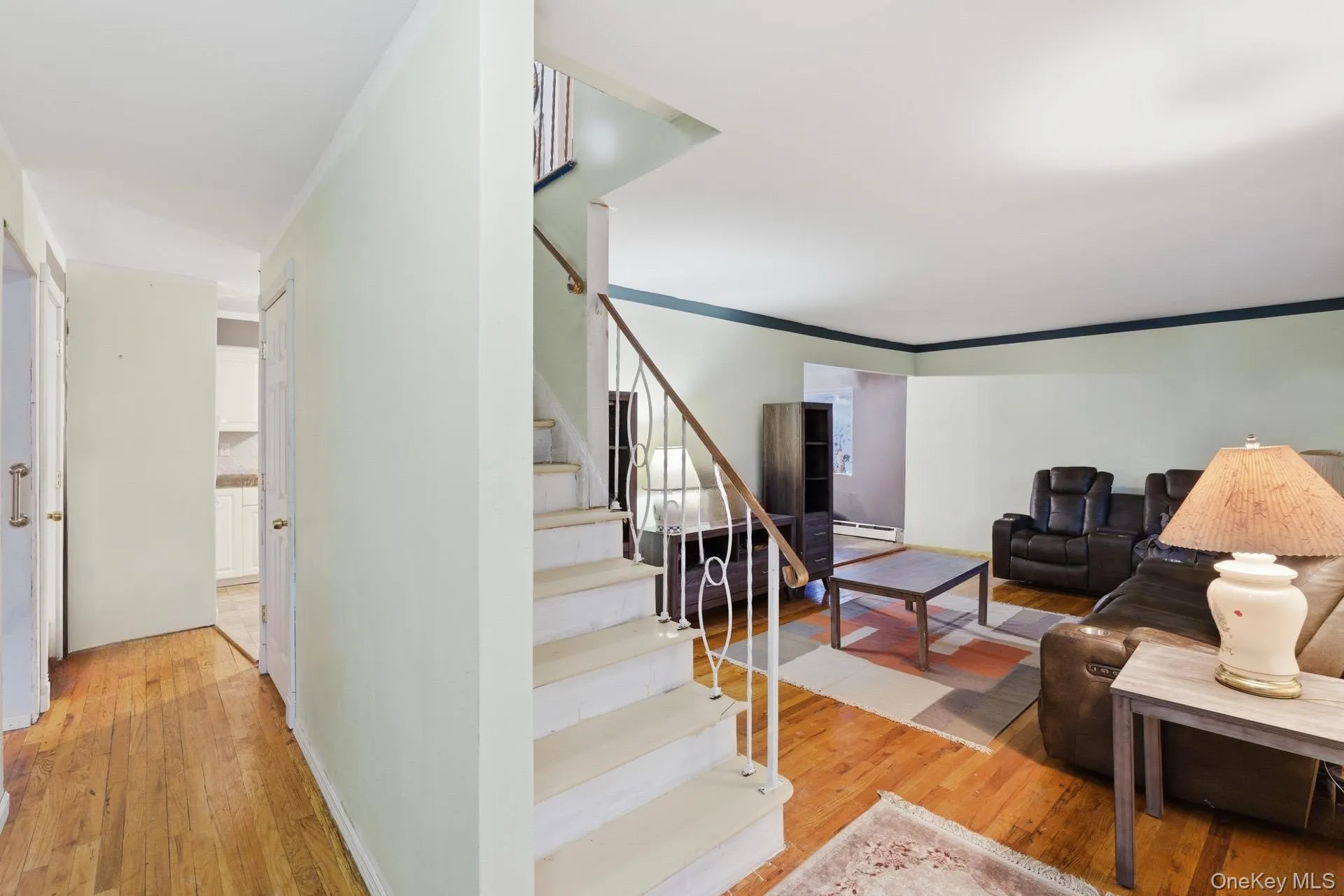 Living room featuring light wood finished floors, ornamental molding, stairway, and a baseboard radiator Living room featuring light wood finished floors, ornamental molding, stairway, and a baseboard radiator