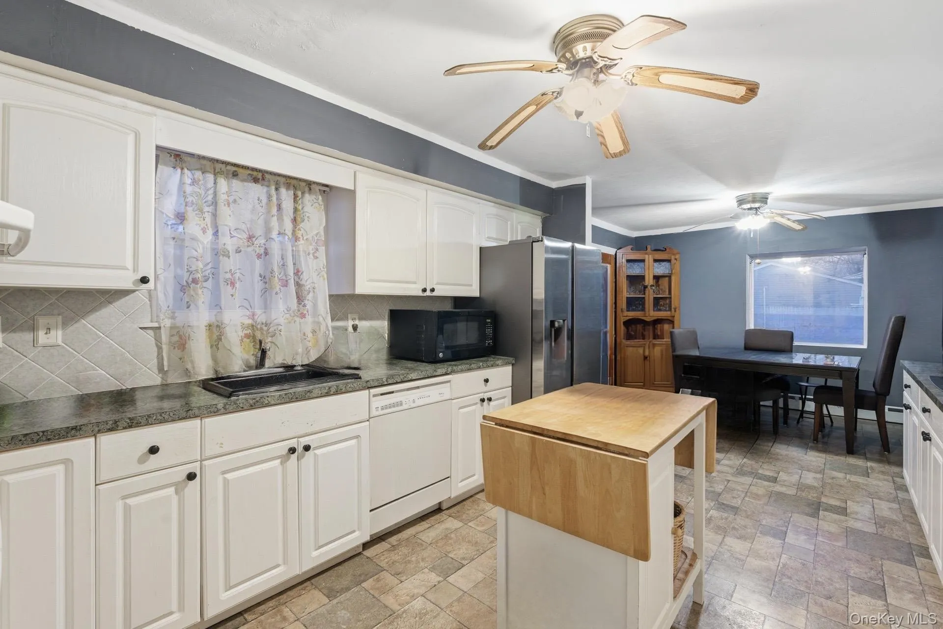 Kitchen featuring dishwasher, dark countertops, stone finish flooring, decorative backsplash, and black microwave Kitchen featuring dishwasher, dark countertops, stone finish flooring, decorative backsplash, and black microwave