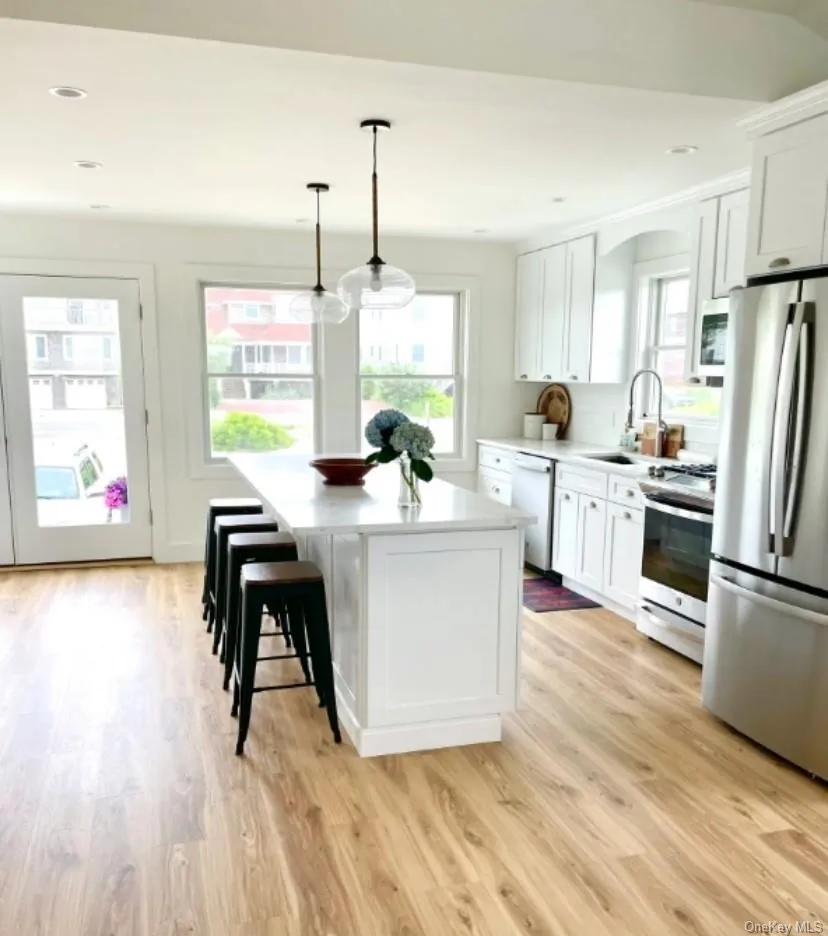 Kitchen with appliances with stainless steel finishes, pendant lighting, white cabinets, a center island, and a breakfast bar Kitchen with appliances with stainless steel finishes, pendant lighting, white cabinets, a center island, and a breakfast bar