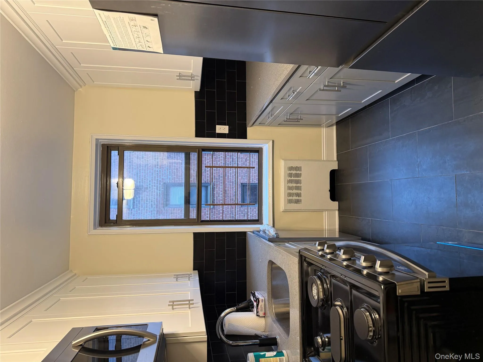 Kitchen featuring appliances with stainless steel finishes, light stone counters, white cabinetry, radiator, and decorative backsplash Kitchen featuring appliances with stainless steel finishes, light stone counters, white cabinetry, radiator, and decorative backsplash