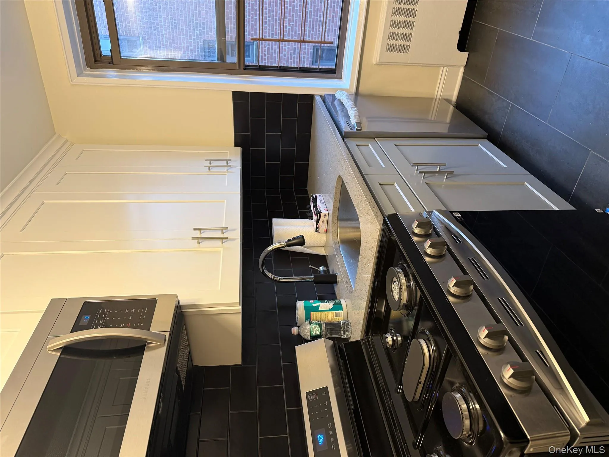 Kitchen with stainless steel range, white cabinets, radiator heating unit, light stone counters, and black dishwasher Kitchen with stainless steel range, white cabinets, radiator heating unit, light stone counters, and black dishwasher