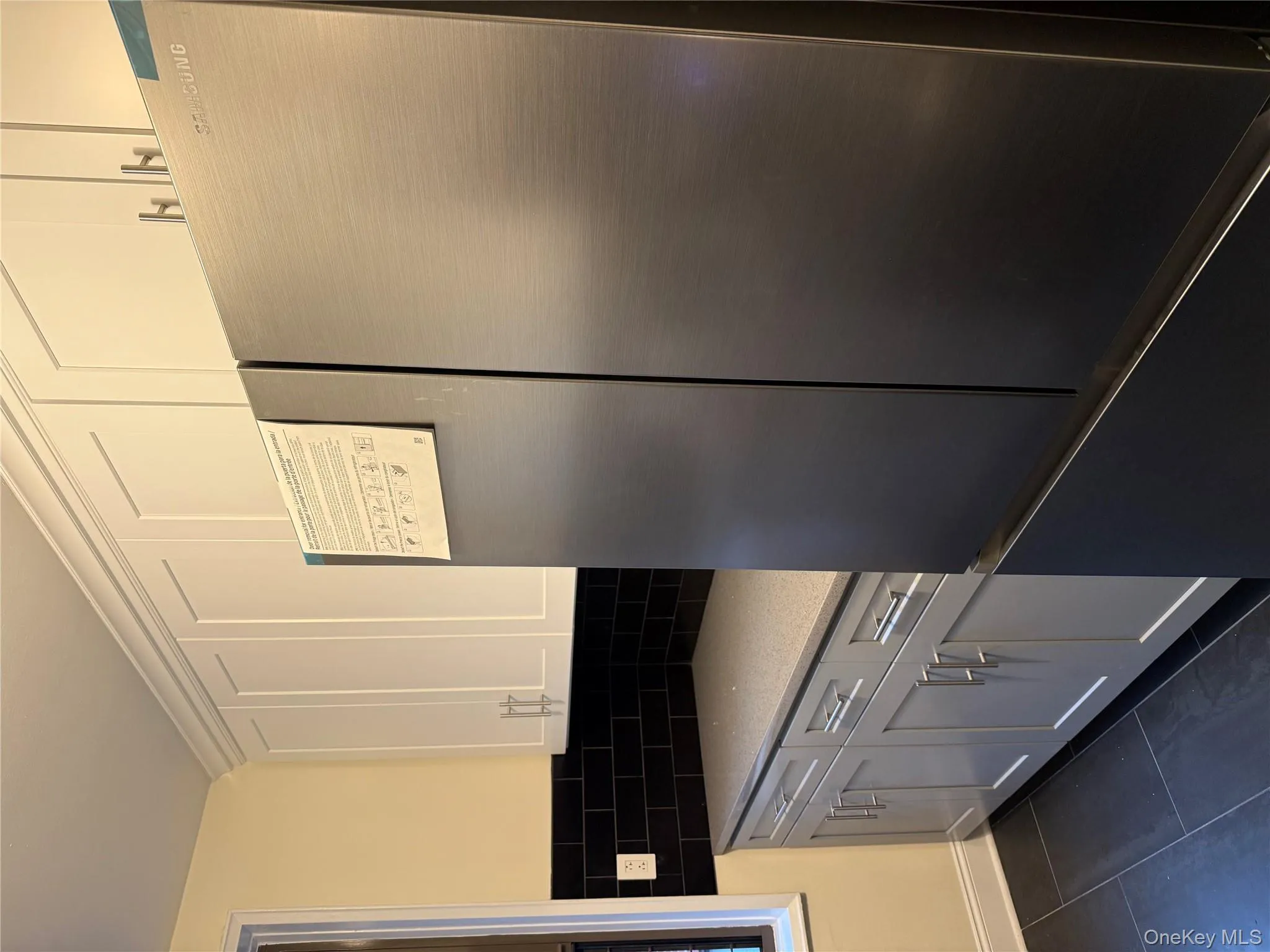 Kitchen featuring stainless steel fridge, light stone countertops, dark tile patterned floors, white cabinetry, and decorative backsplash Kitchen featuring stainless steel fridge, light stone countertops, dark tile patterned floors, white cabinetry, and decorative backsplash