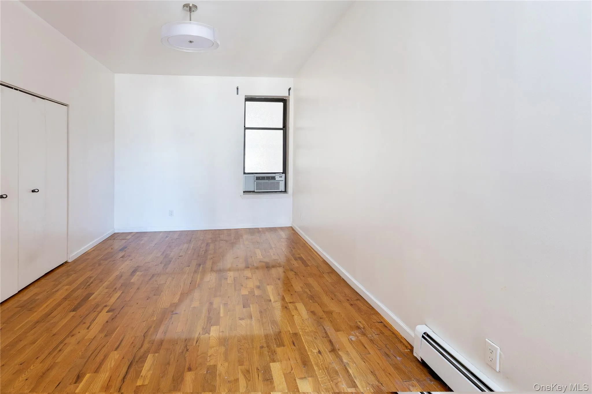 Unfurnished bedroom with a baseboard radiator, hardwood / wood-style flooring, and a closet Unfurnished bedroom with a baseboard radiator, hardwood / wood-style flooring, and a closet