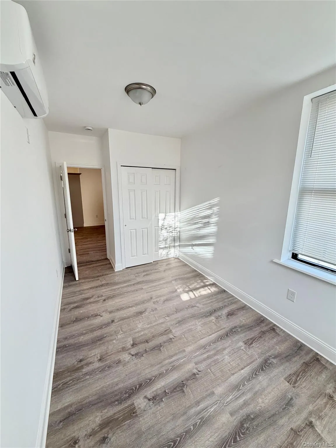 Unfurnished bedroom with light wood-style floors, an AC wall unit, and a closet Unfurnished bedroom with light wood-style floors, an AC wall unit, and a closet