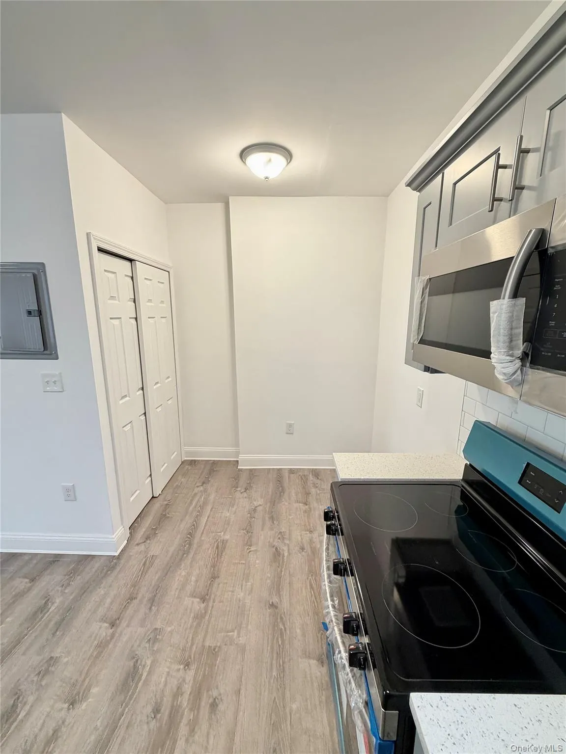 Kitchen featuring stainless steel appliances, electric panel, light wood finished floors, and light stone counters Kitchen featuring stainless steel appliances, electric panel, light wood finished floors, and light stone counters