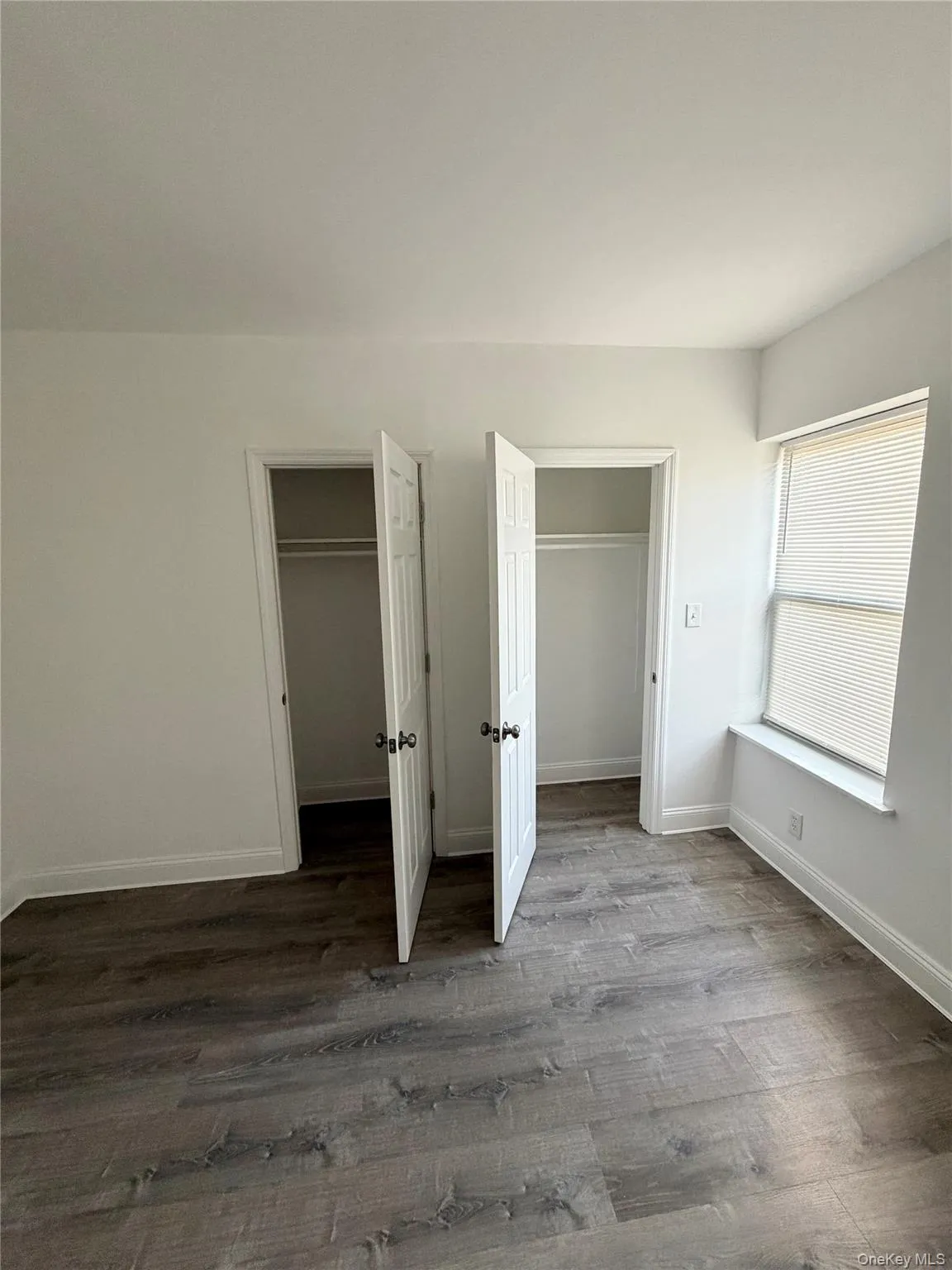Unfurnished bedroom with dark wood-type flooring and two closets Unfurnished bedroom with dark wood-type flooring and two closets