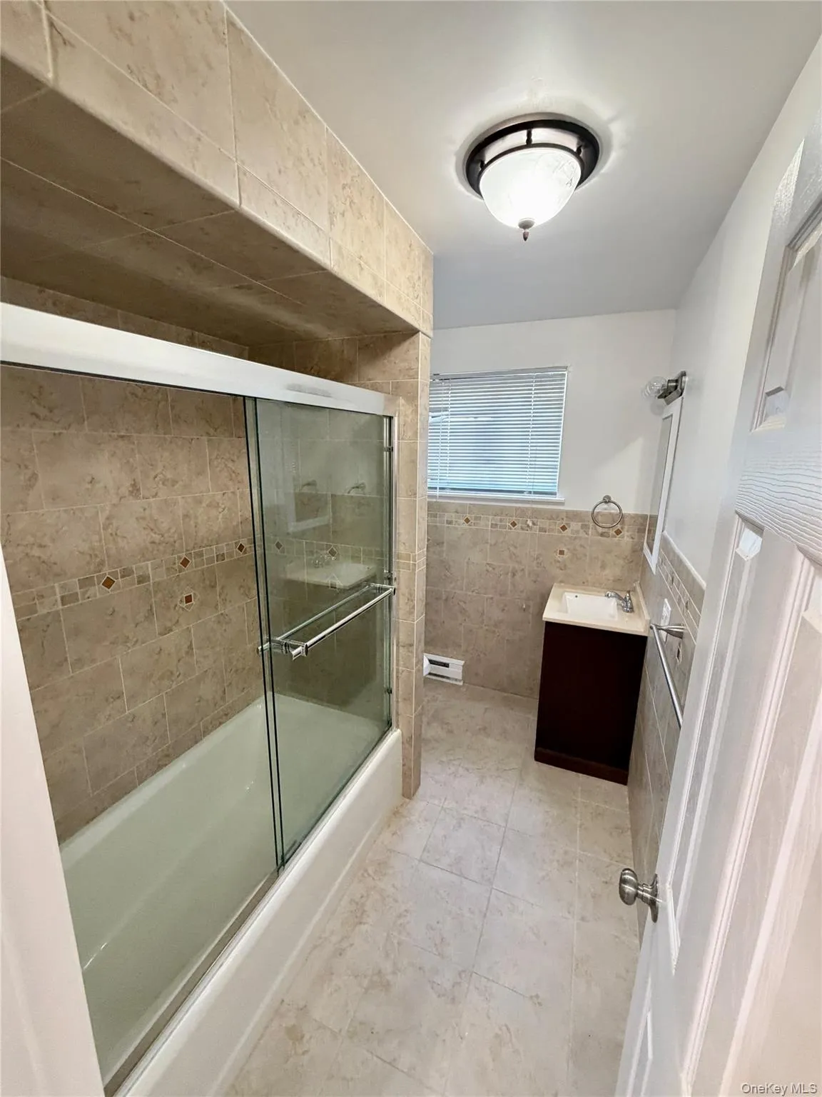 Full bathroom with tile walls, vanity, combined bath / shower with glass door, and light tile patterned floors Full bathroom with tile walls, vanity, combined bath / shower with glass door, and light tile patterned floors