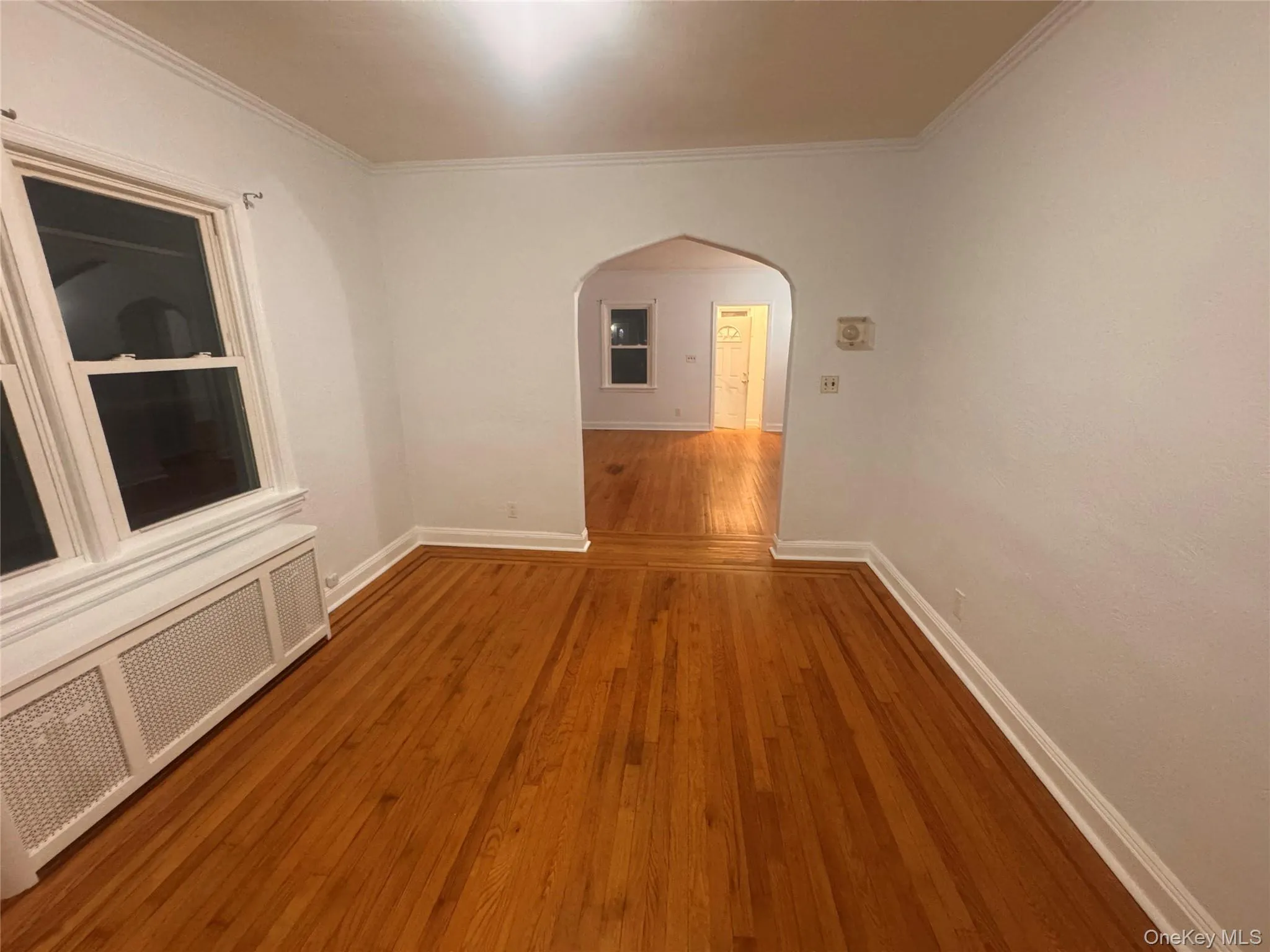 Empty room featuring arched walkways, radiator heating unit, hardwood / wood-style floors, and ornamental molding Empty room featuring arched walkways, radiator heating unit, hardwood / wood-style floors, and ornamental molding