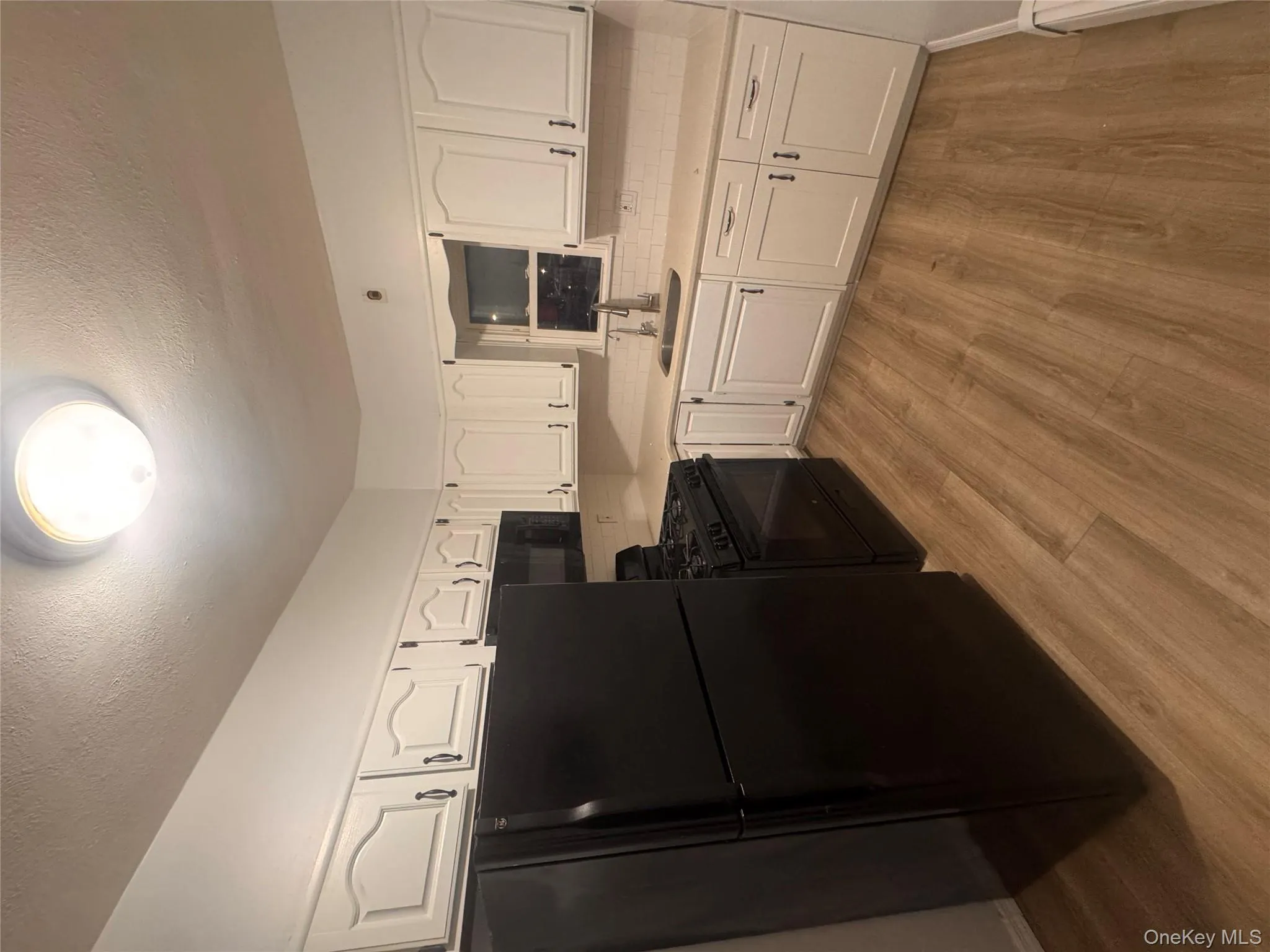 Kitchen featuring fridge, white cabinetry, black range oven, a textured ceiling, and light wood-style flooring Kitchen featuring fridge, white cabinetry, black range oven, a textured ceiling, and light wood-style flooring