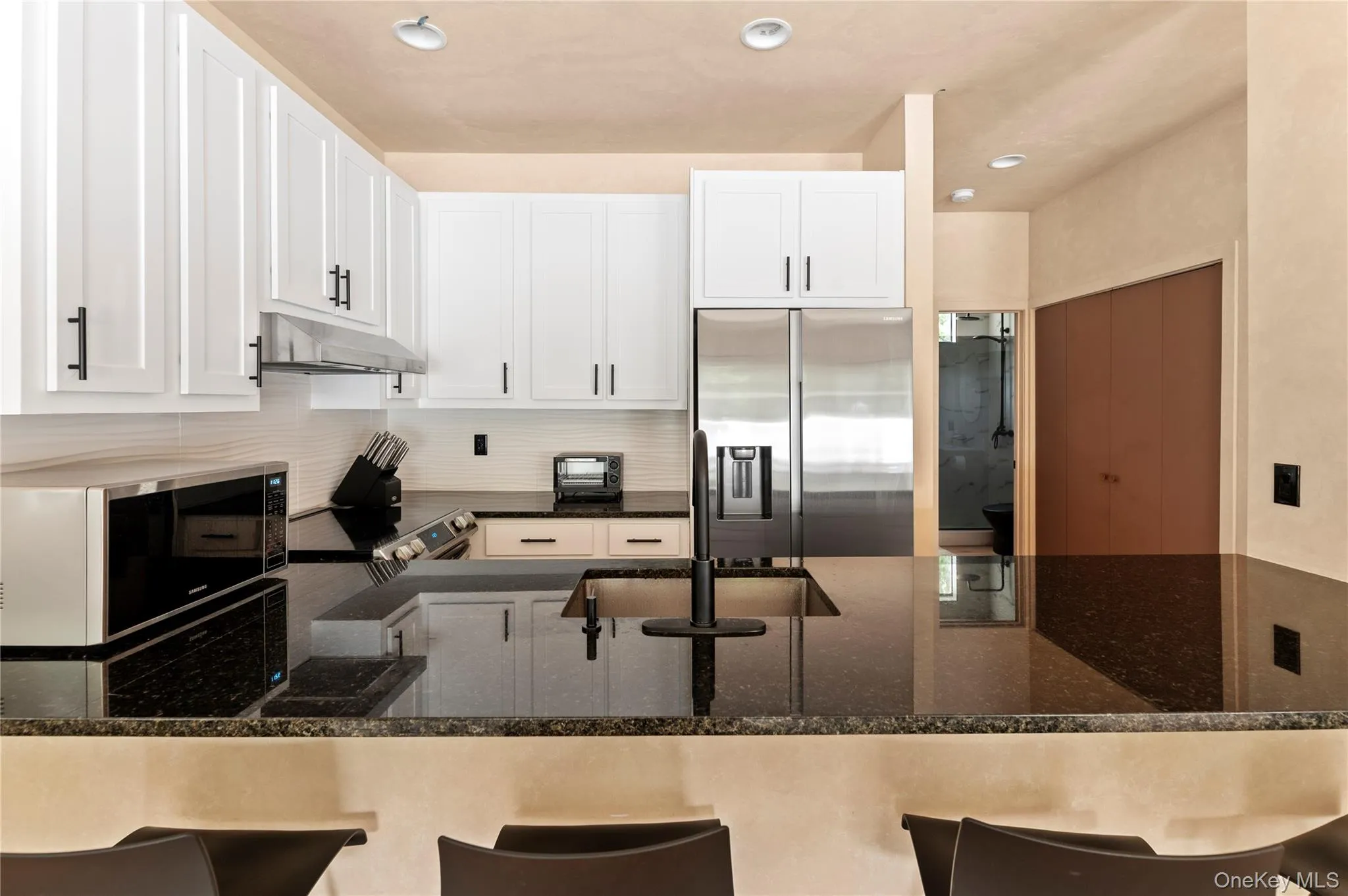 Kitchen with tasteful backsplash, white cabinets, appliances with stainless steel finishes, under cabinet range hood, and a breakfast bar area Kitchen with tasteful backsplash, white cabinets, appliances with stainless steel finishes, under cabinet range hood, and a breakfast bar area