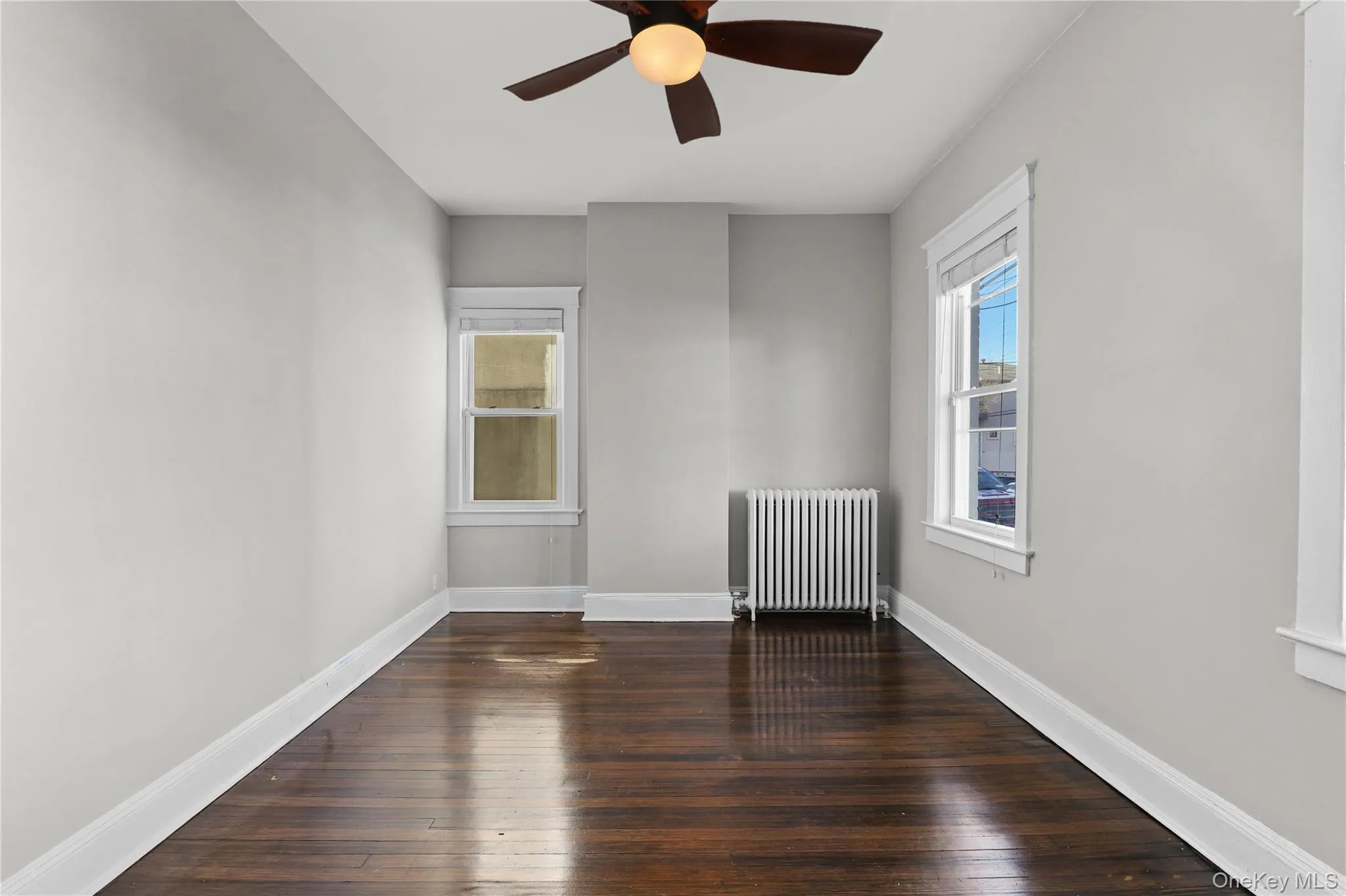 Spare room with radiator heating unit, dark wood-style flooring, and ceiling fan Spare room with radiator heating unit, dark wood-style flooring, and ceiling fan