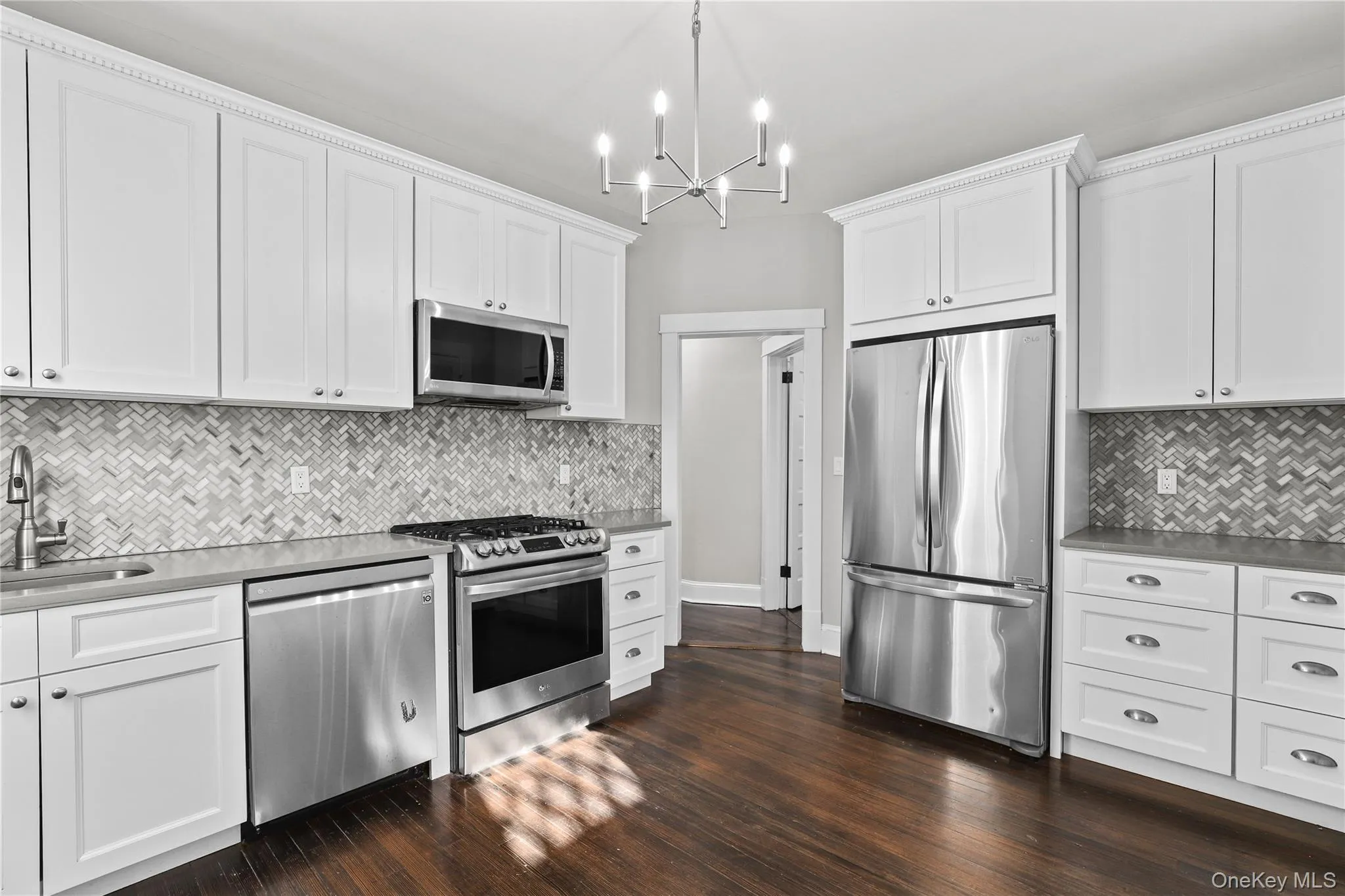 Kitchen with appliances with stainless steel finishes, white cabinetry, and dark wood-style flooring Kitchen with appliances with stainless steel finishes, white cabinetry, and dark wood-style flooring