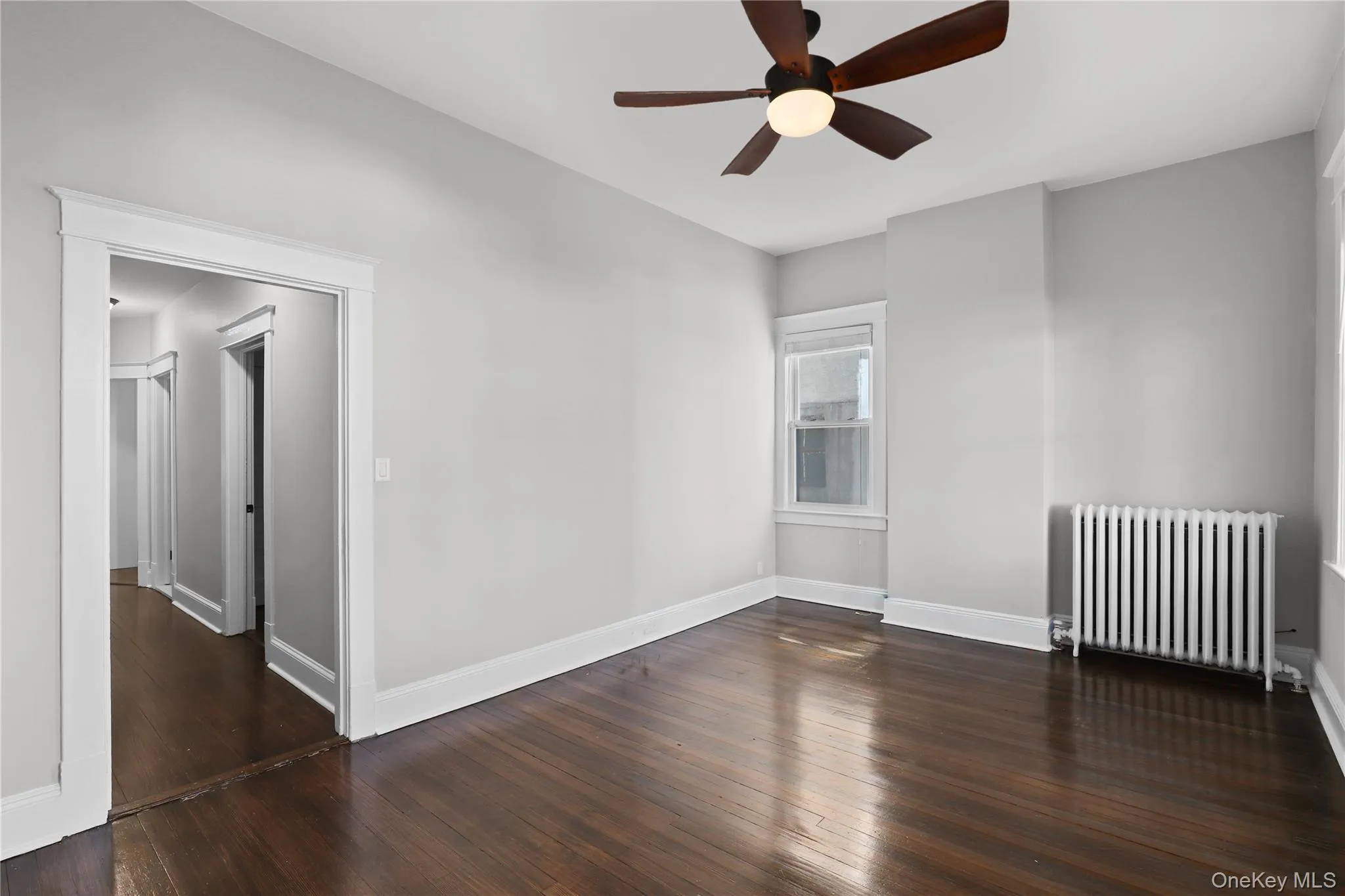 Spare room featuring radiator heating unit, dark wood-style floors, and ceiling fan Spare room featuring radiator heating unit, dark wood-style floors, and ceiling fan