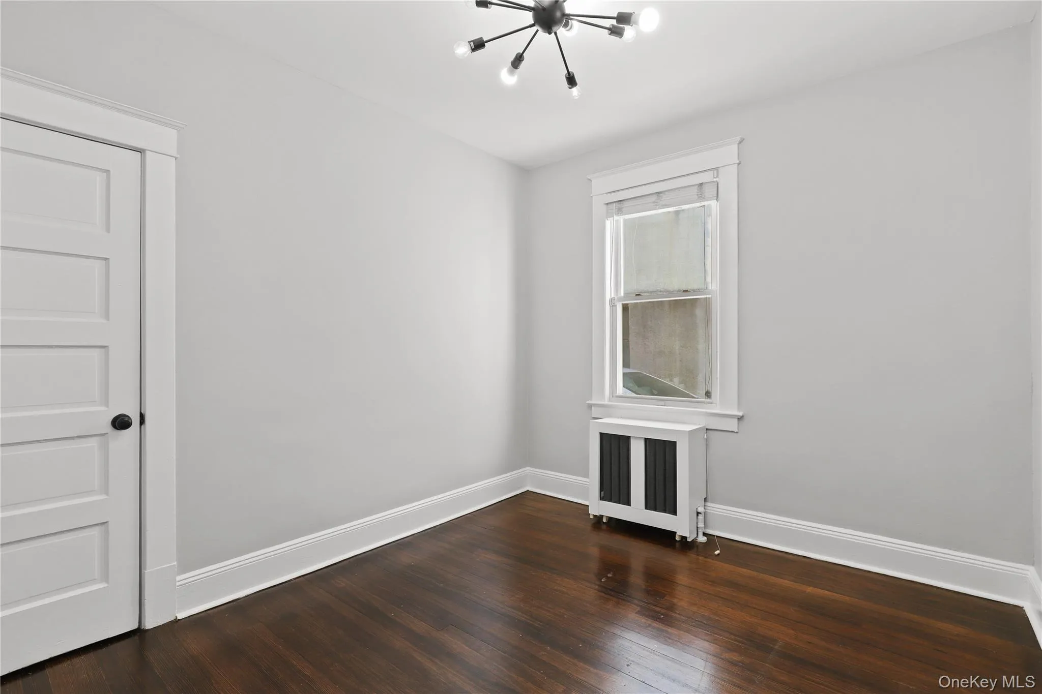 Empty room featuring a chandelier, radiator heating unit, and dark wood-style flooring Empty room featuring a chandelier, radiator heating unit, and dark wood-style flooring