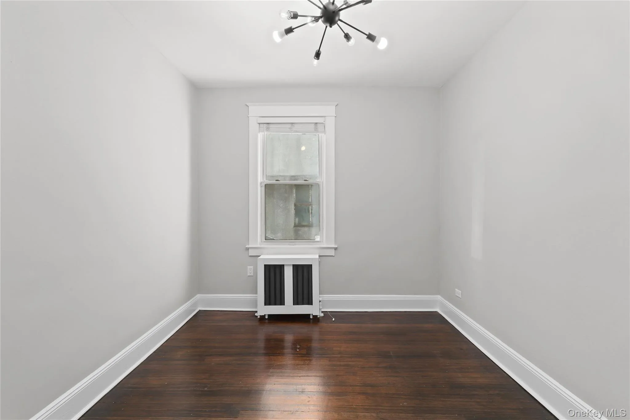 Empty room featuring radiator, a chandelier, and dark wood-style floors Empty room featuring radiator, a chandelier, and dark wood-style floors