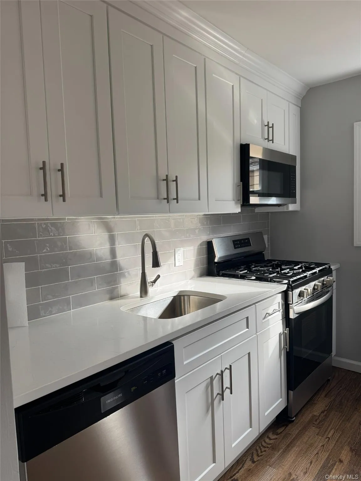 Kitchen featuring stainless steel appliances, light stone counters, dark wood finished floors, backsplash, and white cabinetry Kitchen featuring stainless steel appliances, light stone counters, dark wood finished floors, backsplash, and white cabinetry