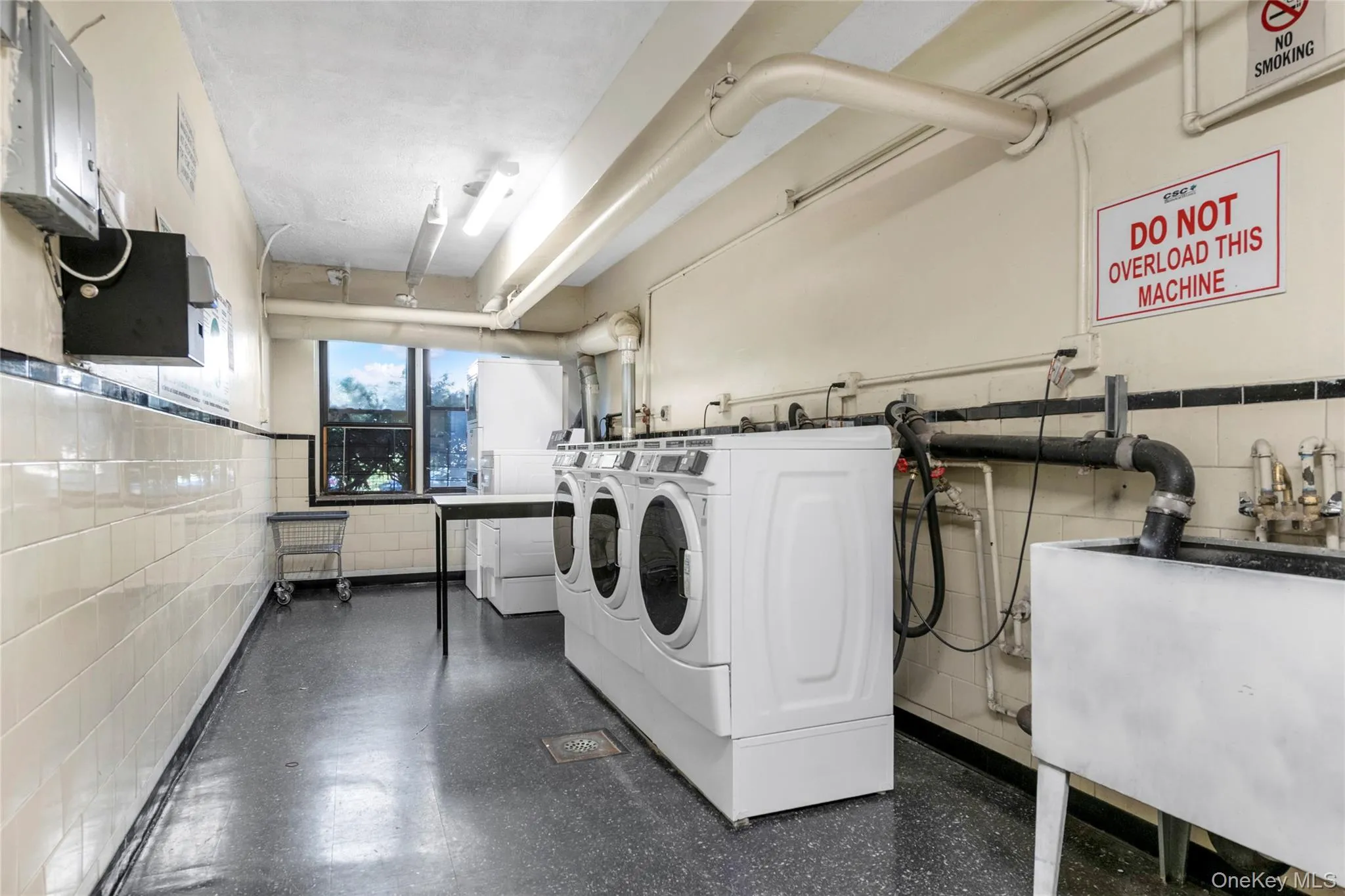 Shared laundry featuring a wainscoted wall, tile walls, washing machine and dryer, and electric panel Shared laundry featuring a wainscoted wall, tile walls, washing machine and dryer, and electric panel