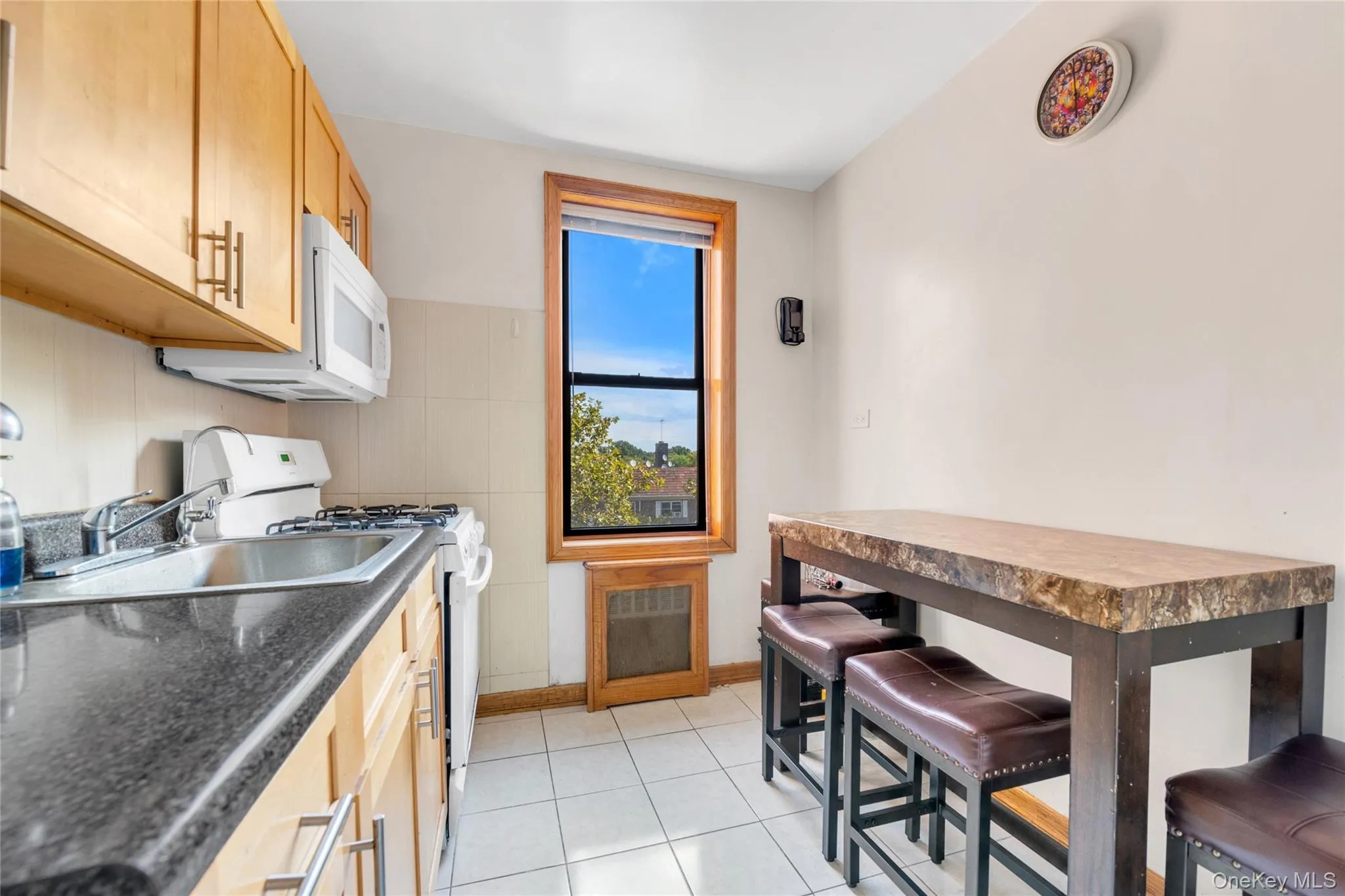 Kitchen featuring white appliances, dark countertops, light brown cabinetry, and light tile patterned floors Kitchen featuring white appliances, dark countertops, light brown cabinetry, and light tile patterned floors