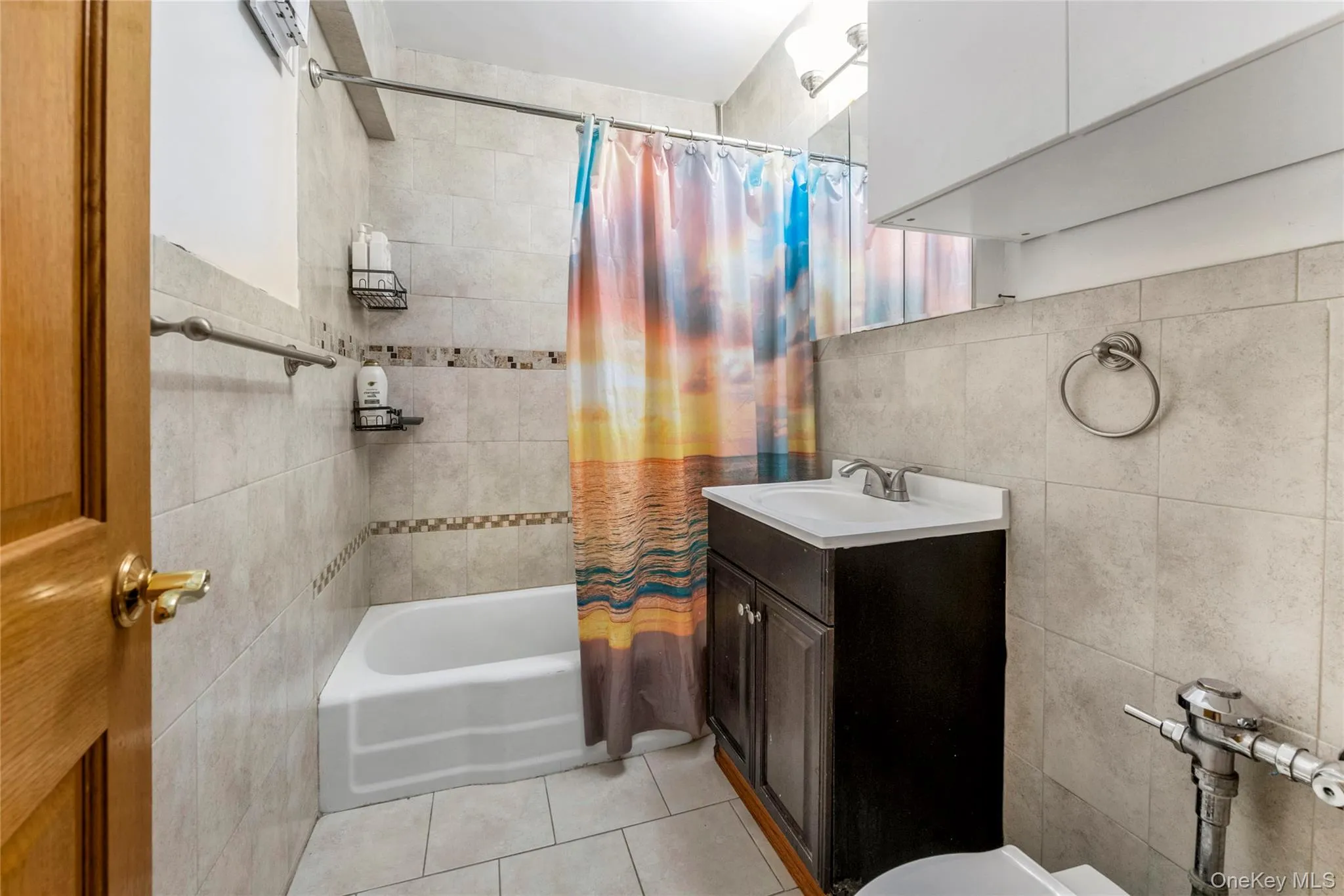 Bathroom featuring vanity, tile walls, shower / tub combo with curtain, and light tile patterned flooring Bathroom featuring vanity, tile walls, shower / tub combo with curtain, and light tile patterned flooring