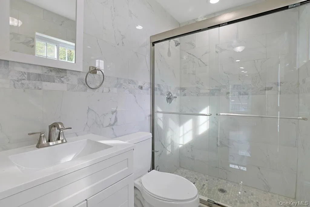 Full bathroom featuring tile walls, a marble finish shower, and vanity Full bathroom featuring tile walls, a marble finish shower, and vanity