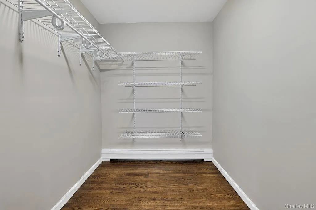 Walk in closet featuring dark wood-style flooring and baseboard heating Walk in closet featuring dark wood-style flooring and baseboard heating