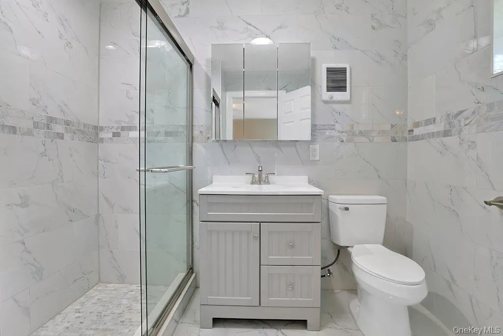 Full bath featuring a marble finish shower, vanity, tile walls, and light marble finish floors Full bath featuring a marble finish shower, vanity, tile walls, and light marble finish floors