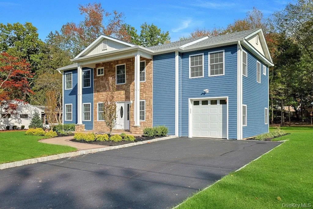 Greek revival inspired property featuring a front yard, stone siding, a garage, and asphalt driveway Greek revival inspired property featuring a front yard, stone siding, a garage, and asphalt driveway