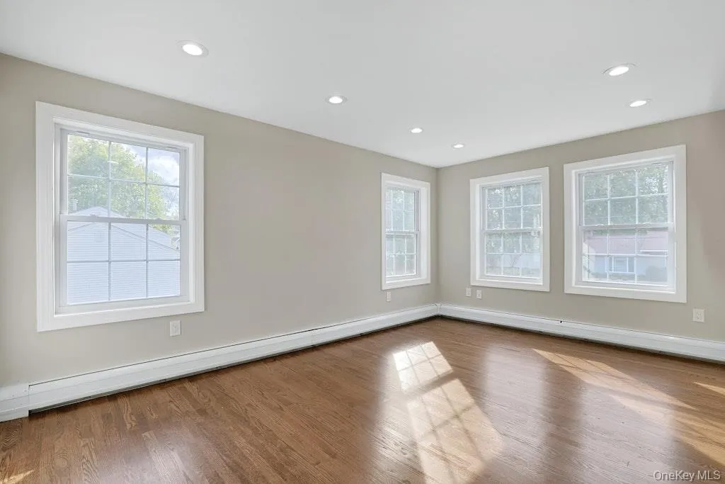 Empty room featuring baseboard heating, plenty of natural light, wood finished floors, and recessed lighting Empty room featuring baseboard heating, plenty of natural light, wood finished floors, and recessed lighting